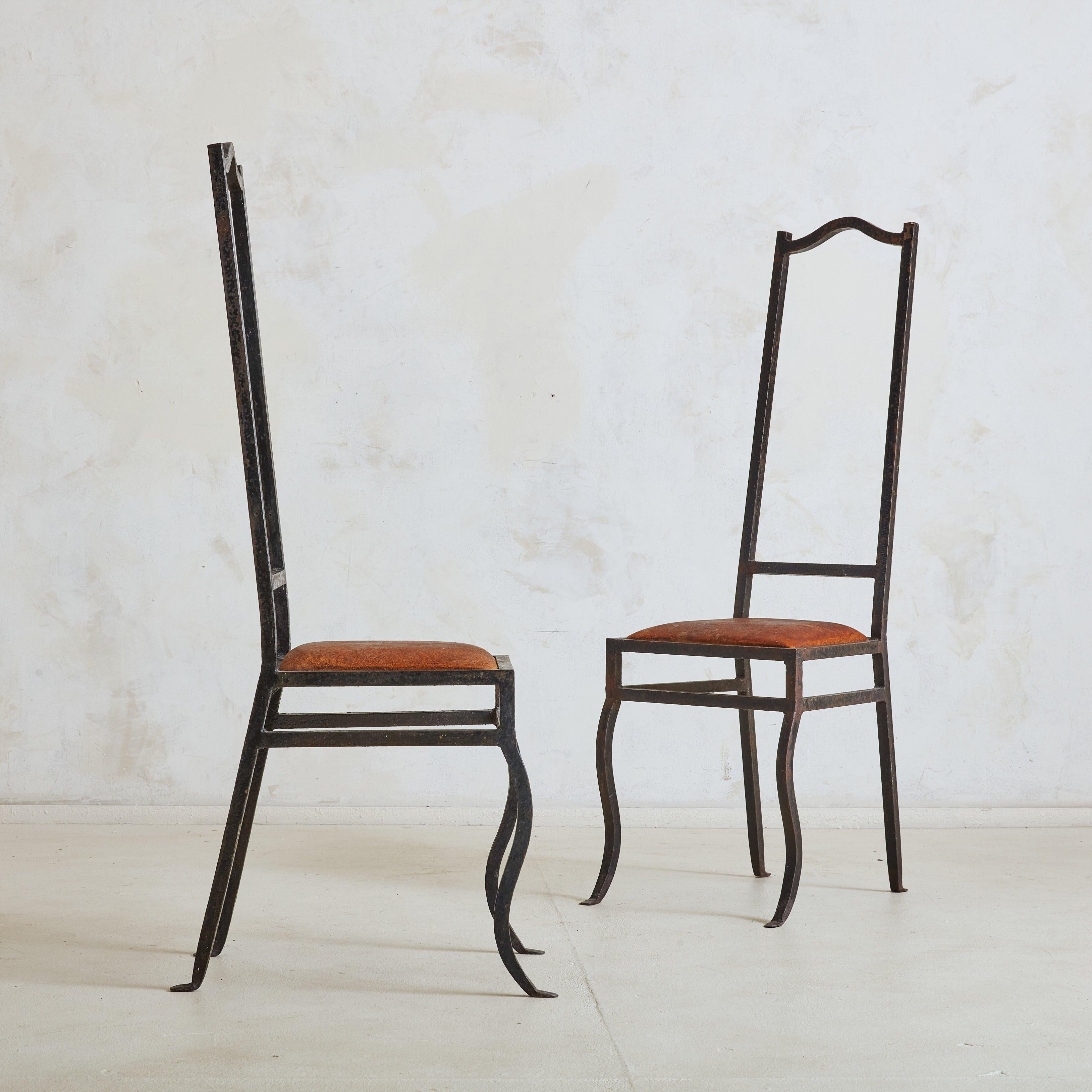 A beautiful pair of 1980s French wrought iron accent chairs featuring tall, narrow backrests and gracefully curved front legs. The frames have a natural patina acquired with age, complemented by seats upholstered in lived-in cognac-hued leather.