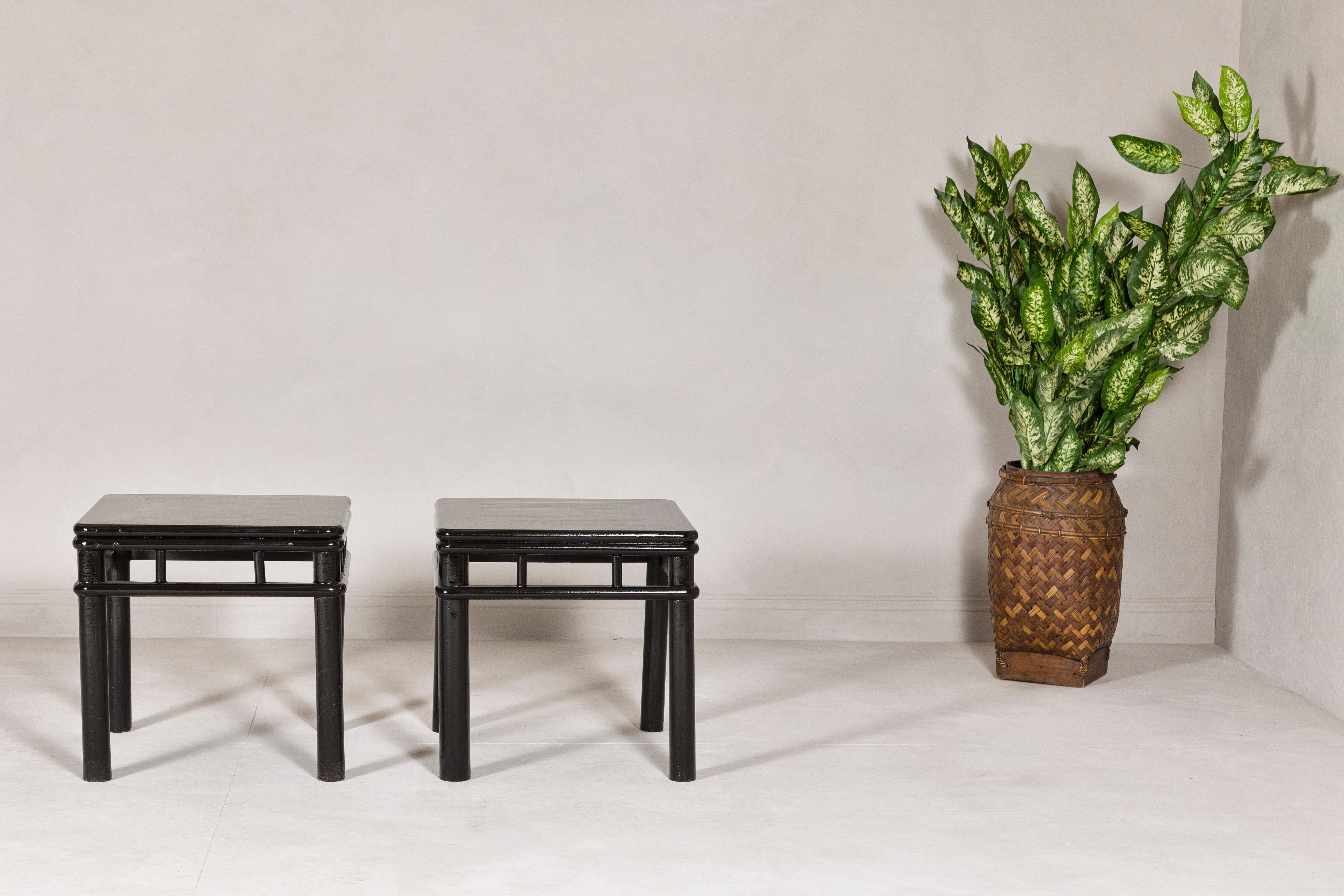 A pair of late Qing Dynasty period black lacquer drinks table from the early 20th century with open stretchers and cylindrical legs. Step into the world of Chinese elegance and history with this pair of late Qing Dynasty black lacquer drinks tables
