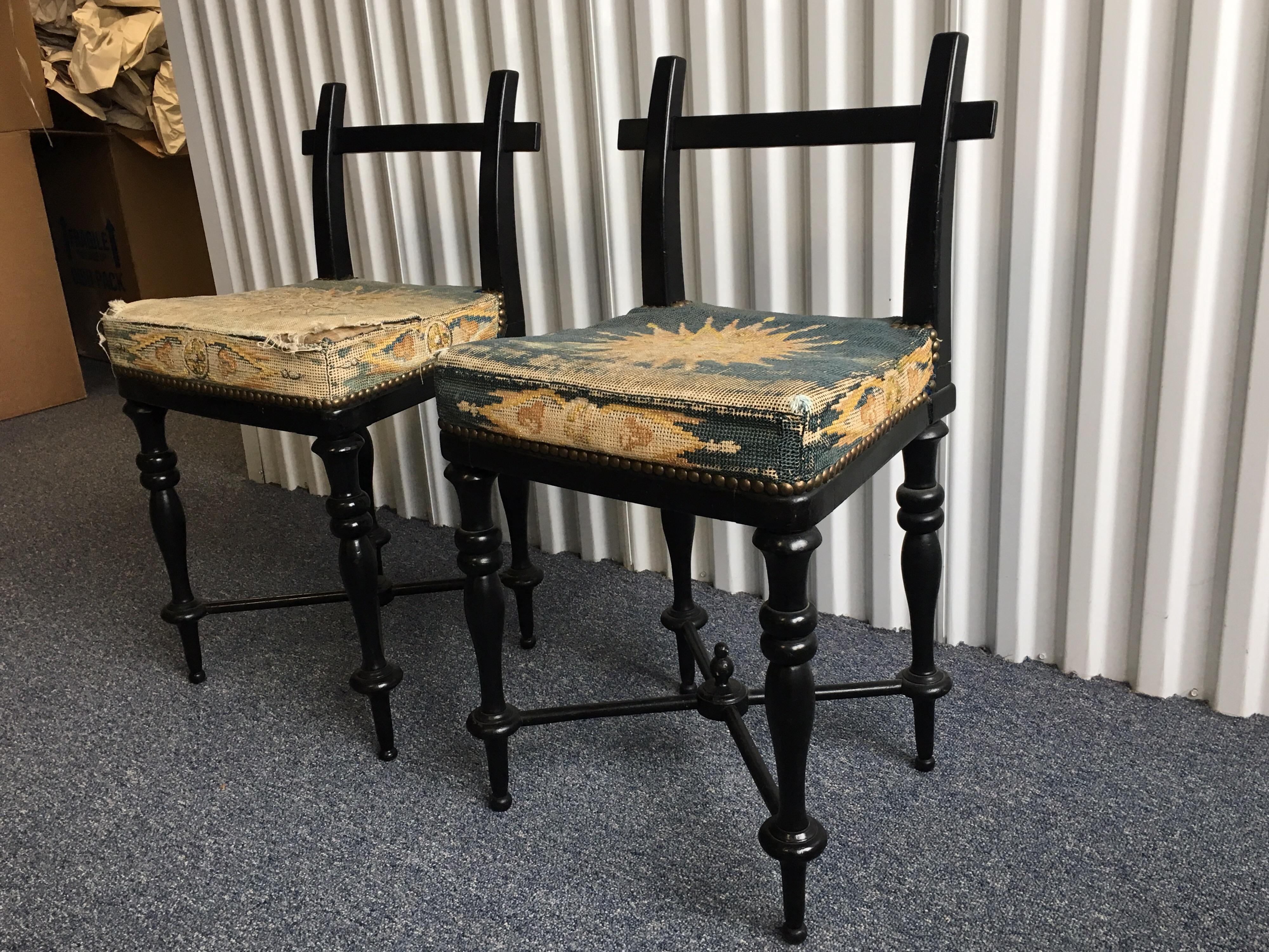 Pair of black lacquered Aesthetic Movement side chairs with worn antique needlepoint sunburst motif upholstered on seat with brass nail heads. Worn needlepoint seats and some missing nail heads.