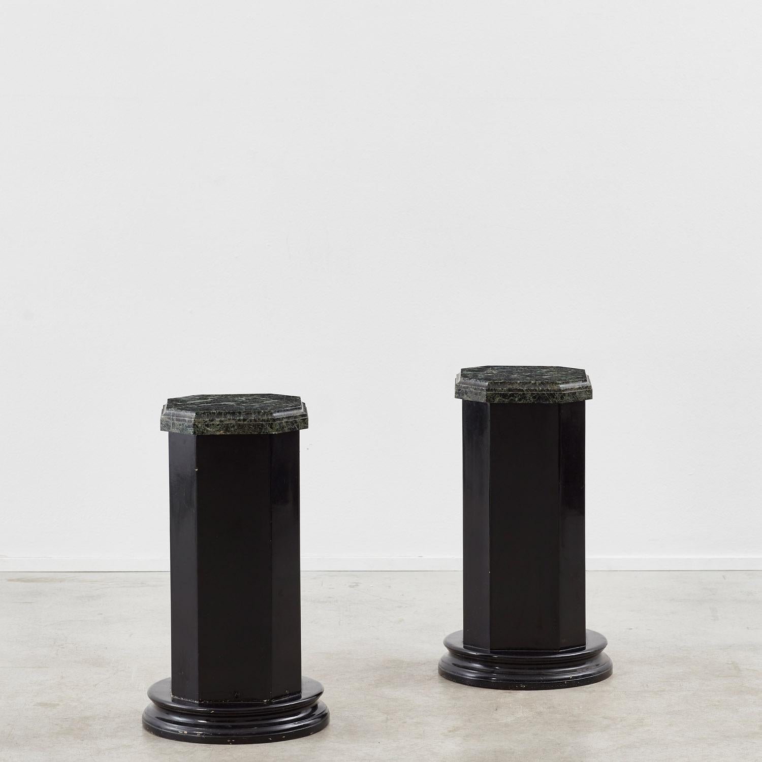 A pair of unusual lacquered columns with a geometric character. Each octagonal column sits on a circular base, and is crowned with a weighty lipped marble top with chamfered detail. 

The columns have been recently restored, with the wood refinished