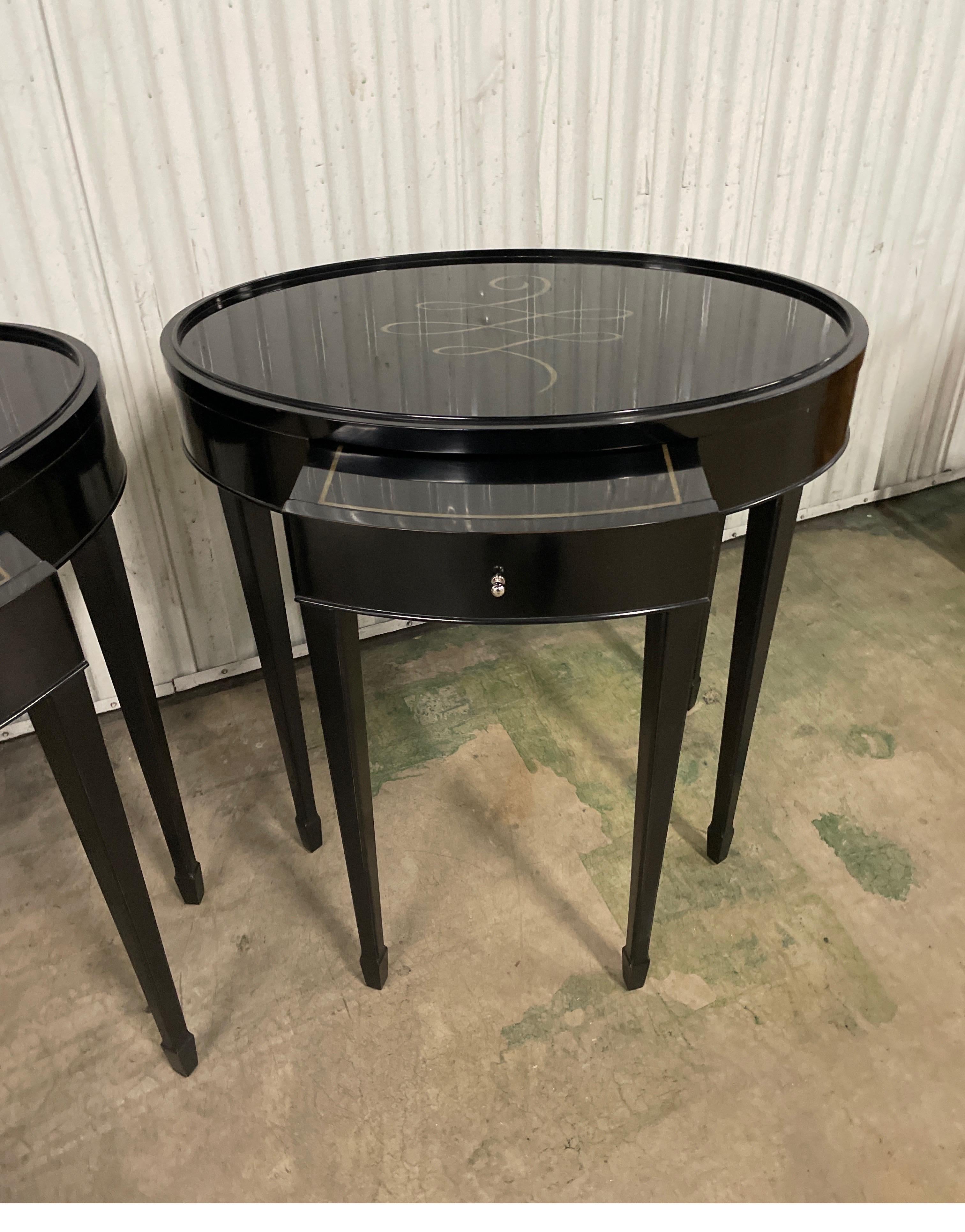 Pair of black lacquered oval end tables with gold calligraphy on the tops. Tables have a small pull-out at front for additional surface. These end tables were designed by Barbara Barry for Baker furniture co.
