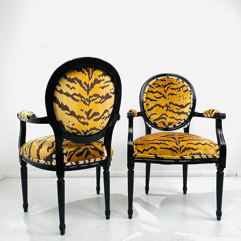 A pair of French Louis XVI style black lacquered accent armchairs upholstered in stunning designer tiger print velvet. This pair of French chairs features oval backs, scrolled and partially upholstered arms, four fluted and tapered legs as well as