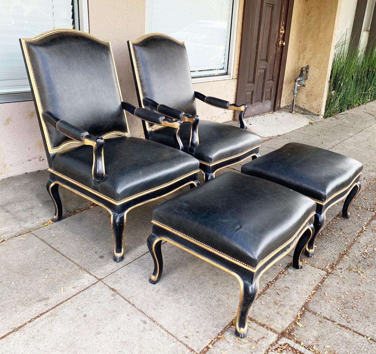Pair of black leather armchairs and ottomans with ebonized wood frames and 18-karat gold leaf accents, carved hoof feet and copper nailhead trimming.

The chairs are in excellent condition, minor nicks to feet/frame but overall in excellent shape,