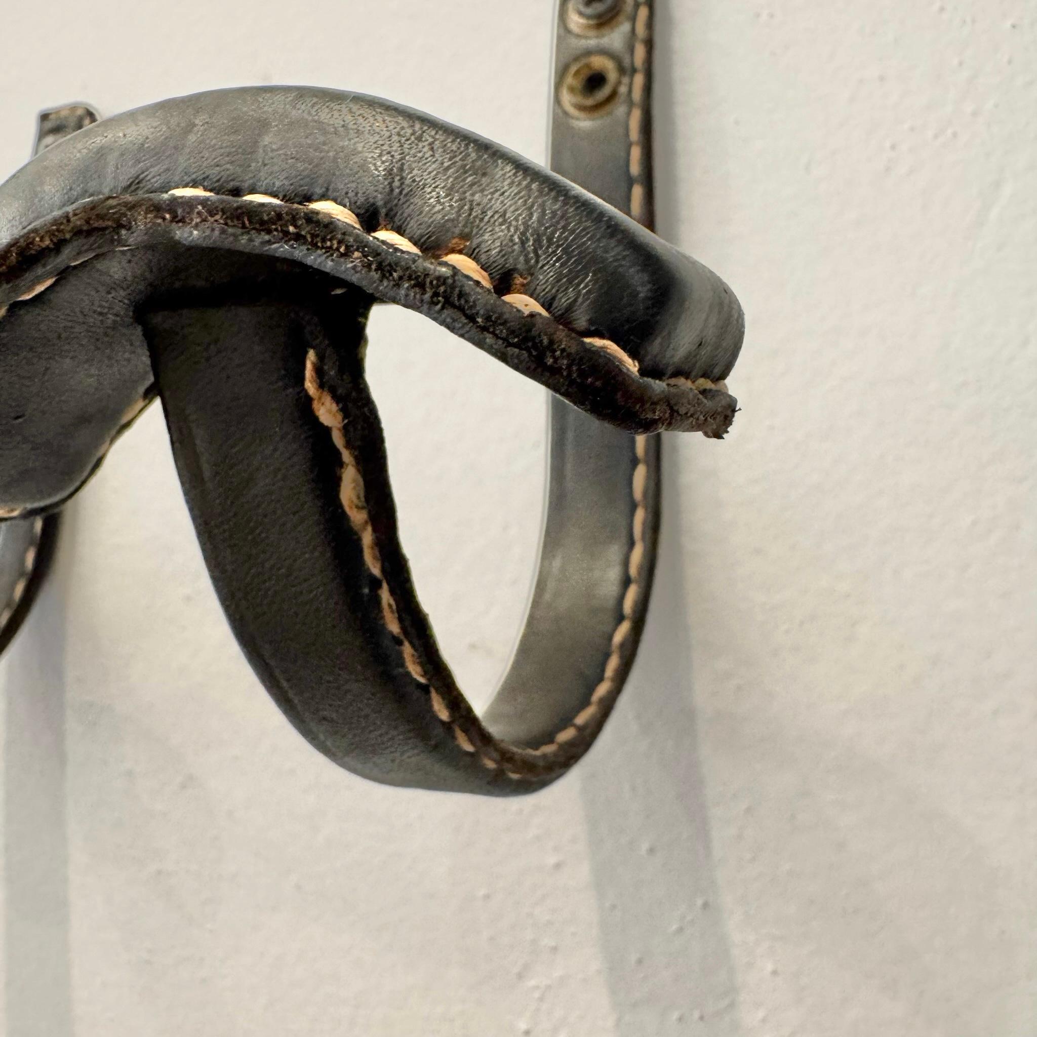 Un classico paio di appendiabiti del designer francese Jacques Adnet. I loro telai in ferro nero e i ganci curvi sono completamente avvolti in pelle nera, con le cuciture a contrasto tipiche di Adnet. Due fori su ogni gancio per il montaggio.  Buone