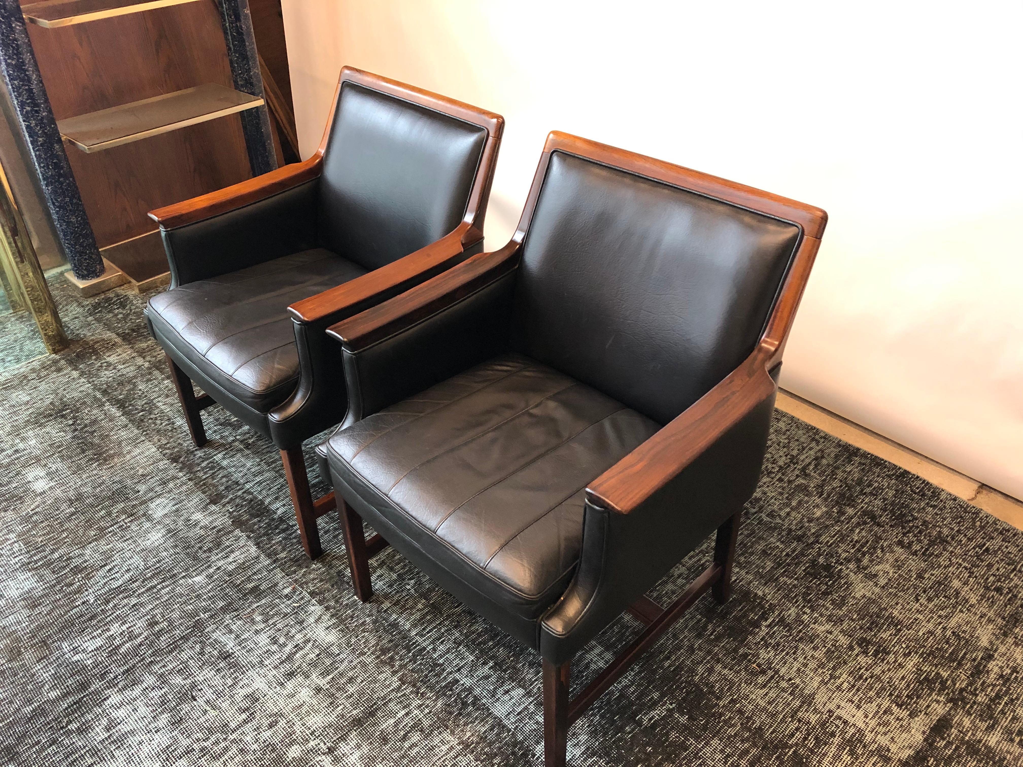 This pair of rosewood and black leather Minerva club chairs by Torbjorn Afdal for Bruksbo are in overall good condition and wear consistent with age and use.  These chairs are crafted of solid Brazilian rosewood and upholstered in original black