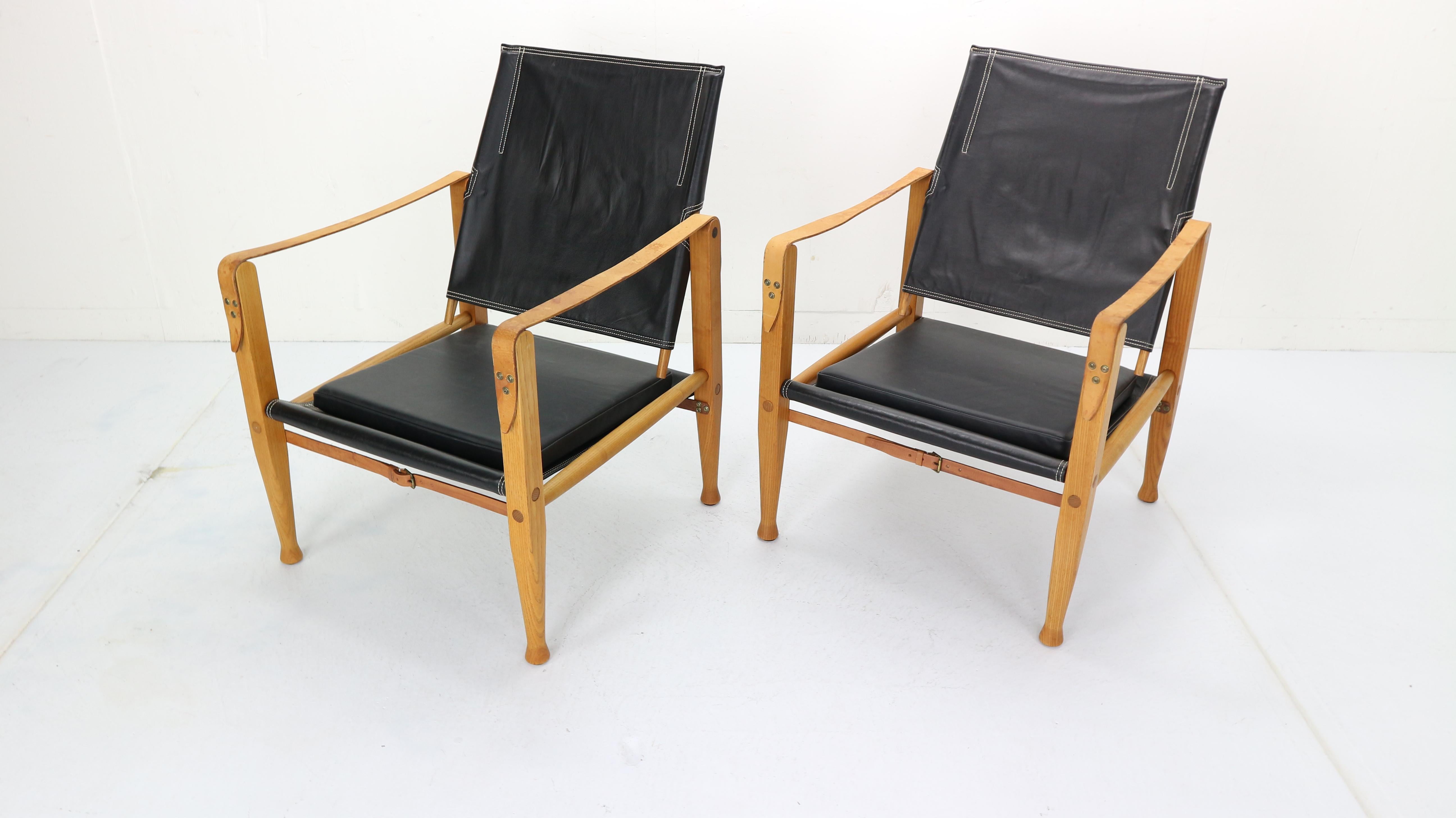 The original Danish safari chairs by Kaare Klint for Rud. Rasmussen.

First produced in 1933, this pair were made in the 1950s from strikingly grained ashwood.

With black leather seat, backrest and cushion, tan leather straps and brass