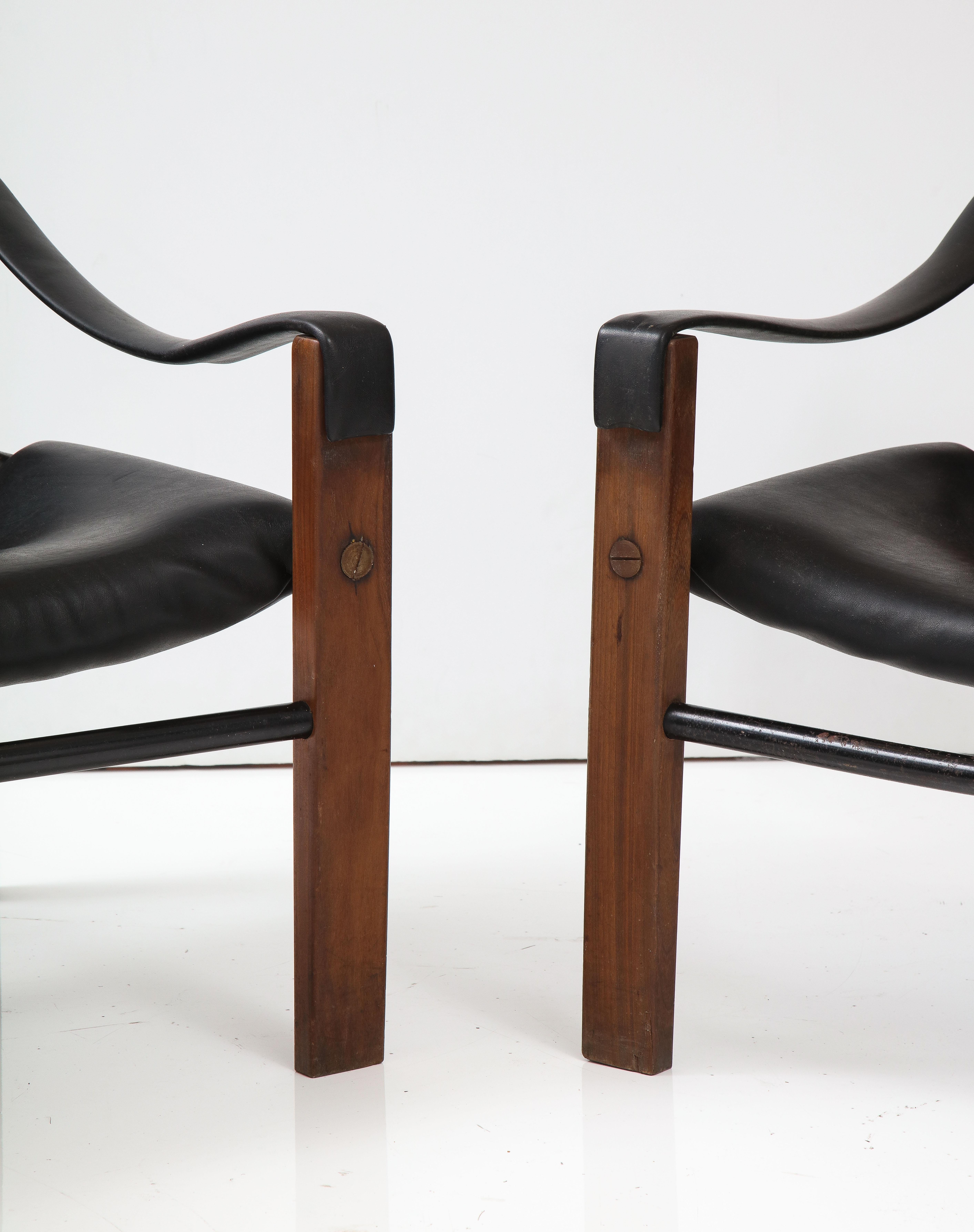 Wonderful pair of vintage teak wood and faux black leather 'Safari' arm chairs supported on black metal frames, designed by Maurice Burke for British furniture manufacturer Arkana, circa 1980. Original upholstery is in excellent condition with small
