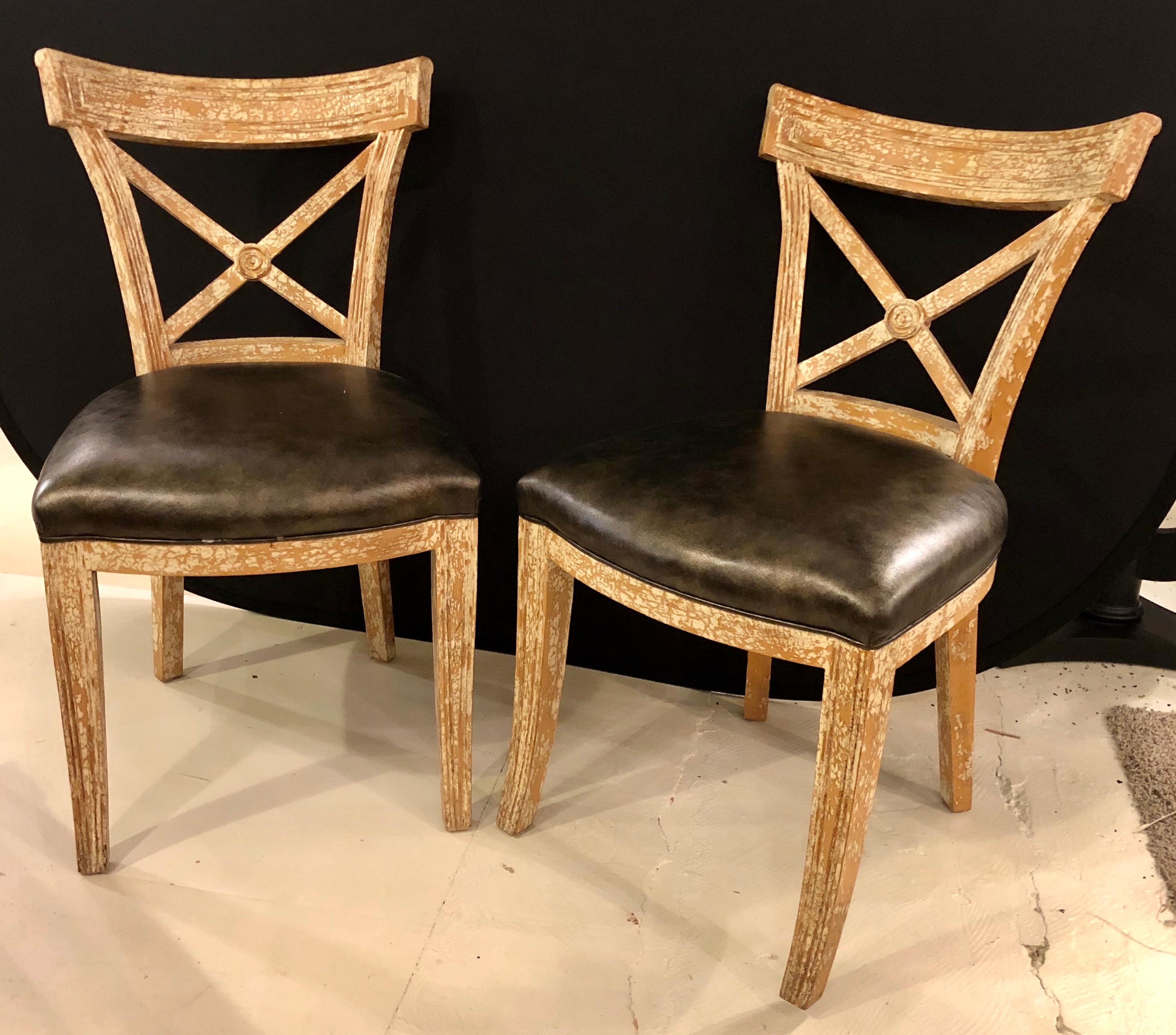 Pair of black leather seat side chairs. Each of these Hollywood Regency side chairs are done in a hand painted crackle-ware finish. The large X-form back rest flowing from a center sphere leading to a black leather seat rest on tapering legs. The