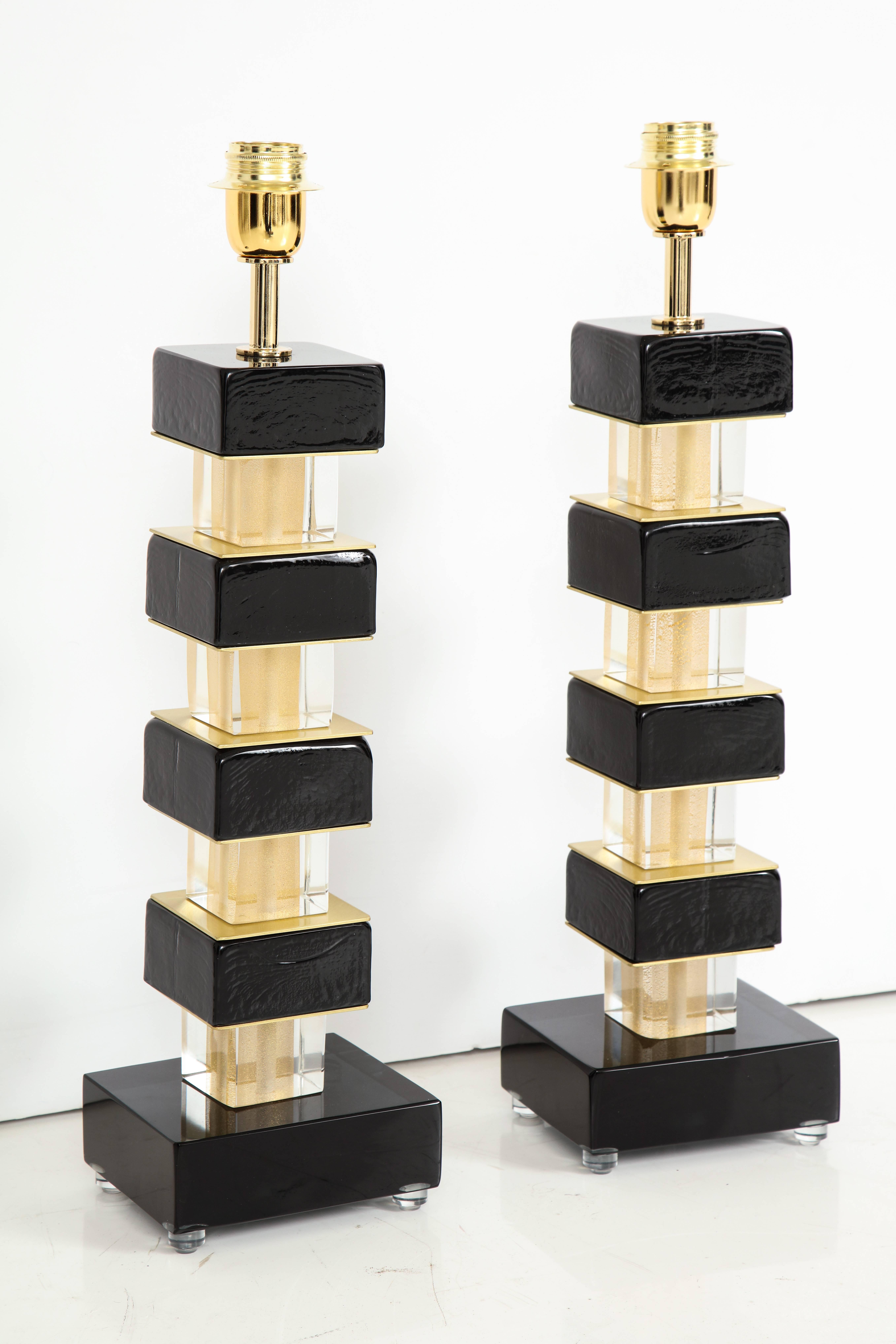 Pair of hand-casted and handcrafted black solid Murano square glass blocks and brass lamps. Individual glass blocks in alternating black and clear with 24-karat gold flecks are separated by brass plates and sit atop a solid black Murano glass block