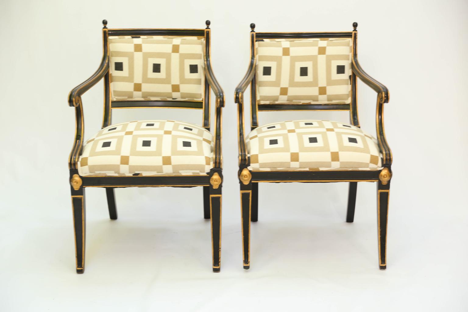 Pair of armchairs, in Regency taste, each having a black painted finish with parcel-gilt accents, their rectangular, padded backrests in molded frame, surmounted by finials, curved arms raised on downswept, reeded terminals, flanking the stuff-over