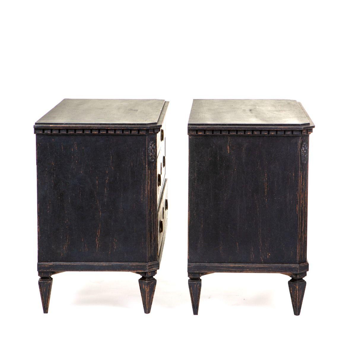 Un par de elegantes cómodas de estilo Gustaviano, fabricadas en pino y pintadas de negro con detalles decorativos en gris claro.
Cada cómoda dispone de tres cajones, el superior adornado con un friso clásico à la grecque. Los cajones inferiores