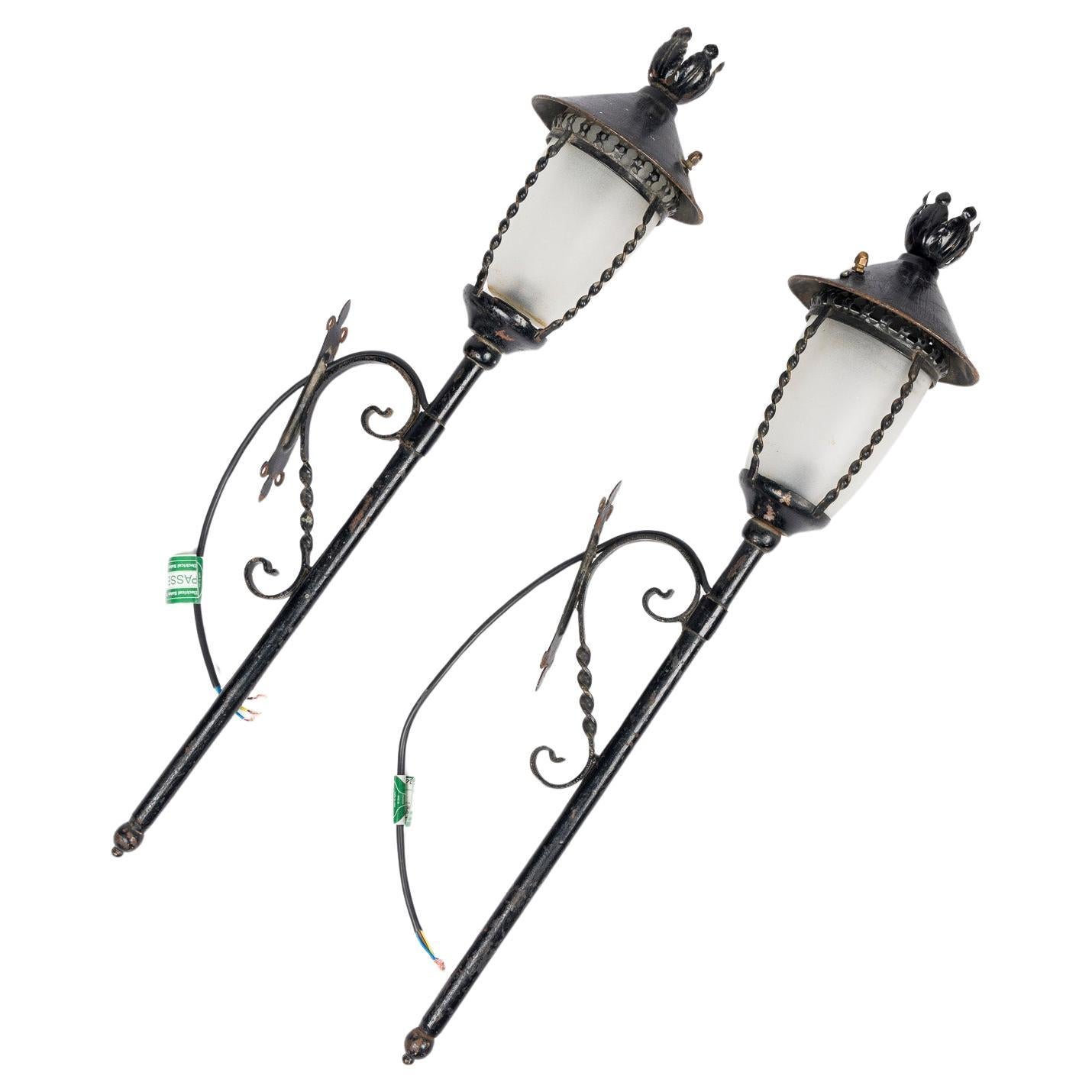 Pair of black painted wrought iron wall lights, with frosted shades.