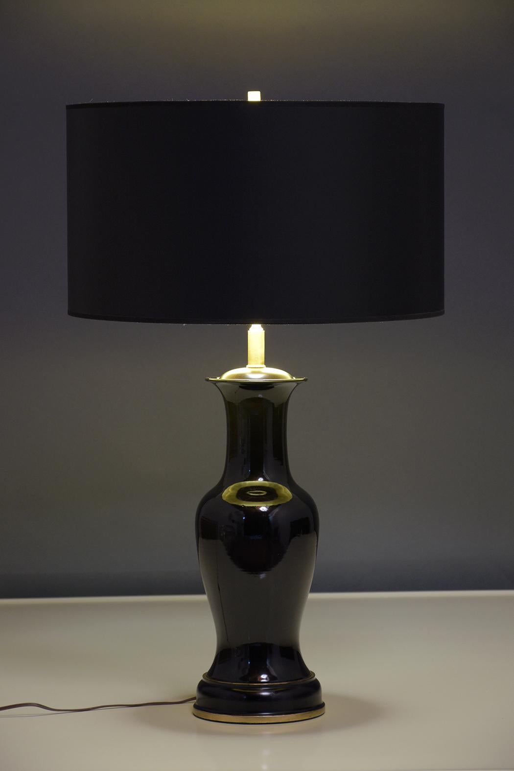 An elegant pair of black porcelain table lamps that have been newly restored by our craftsmen and in working condition. This set of lamps features new matte black color shades and beautiful black porcelain bases that rest on carved wood bases with