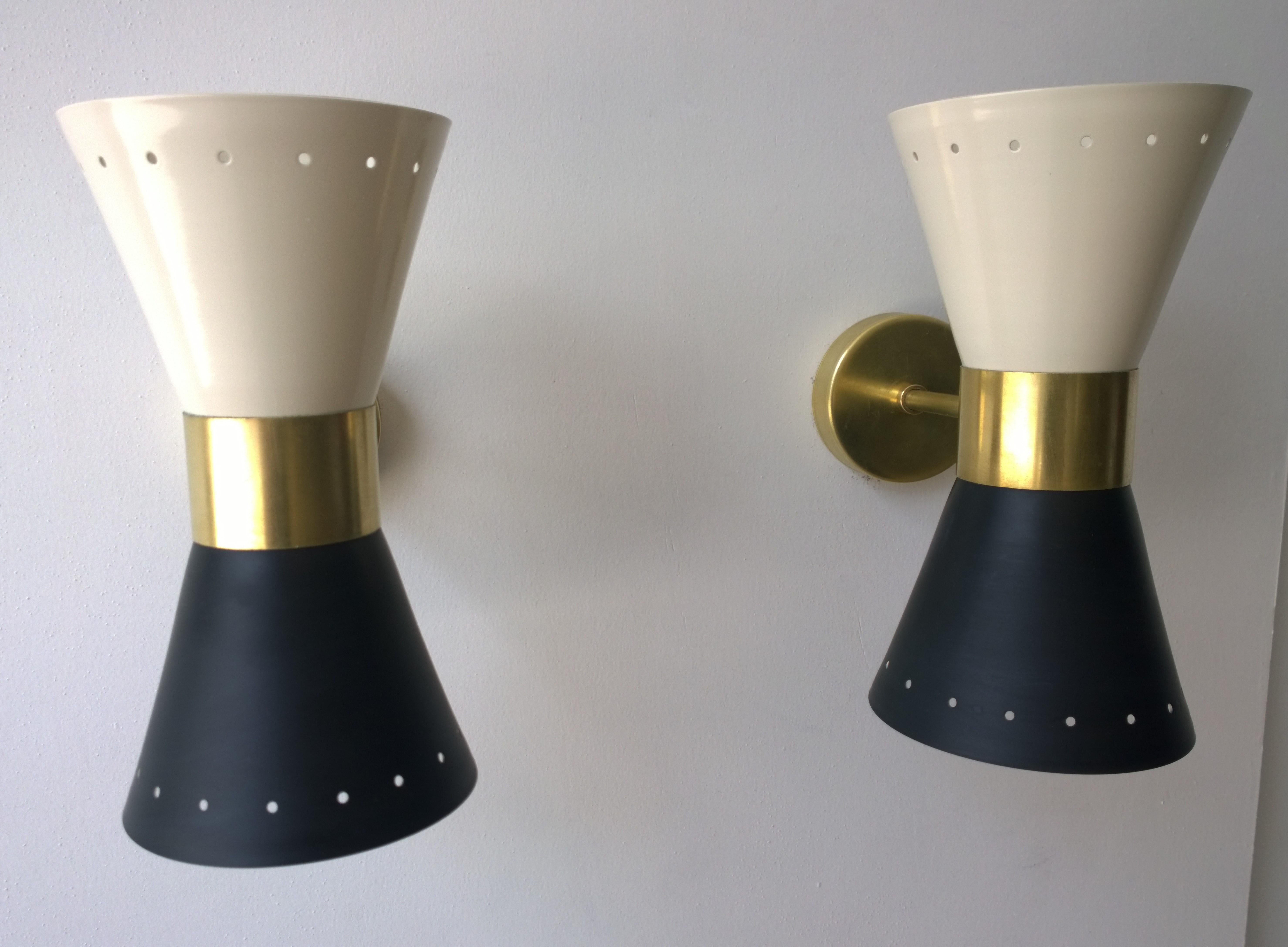 Offered is a pair of Mid-Century Modern Italian Stilnovo style double cone (2 candelabra each) brass enameled in black and white (exterior) with a white (interior) sconces and brass hardware. Each cone has stylized perforations at each end. The