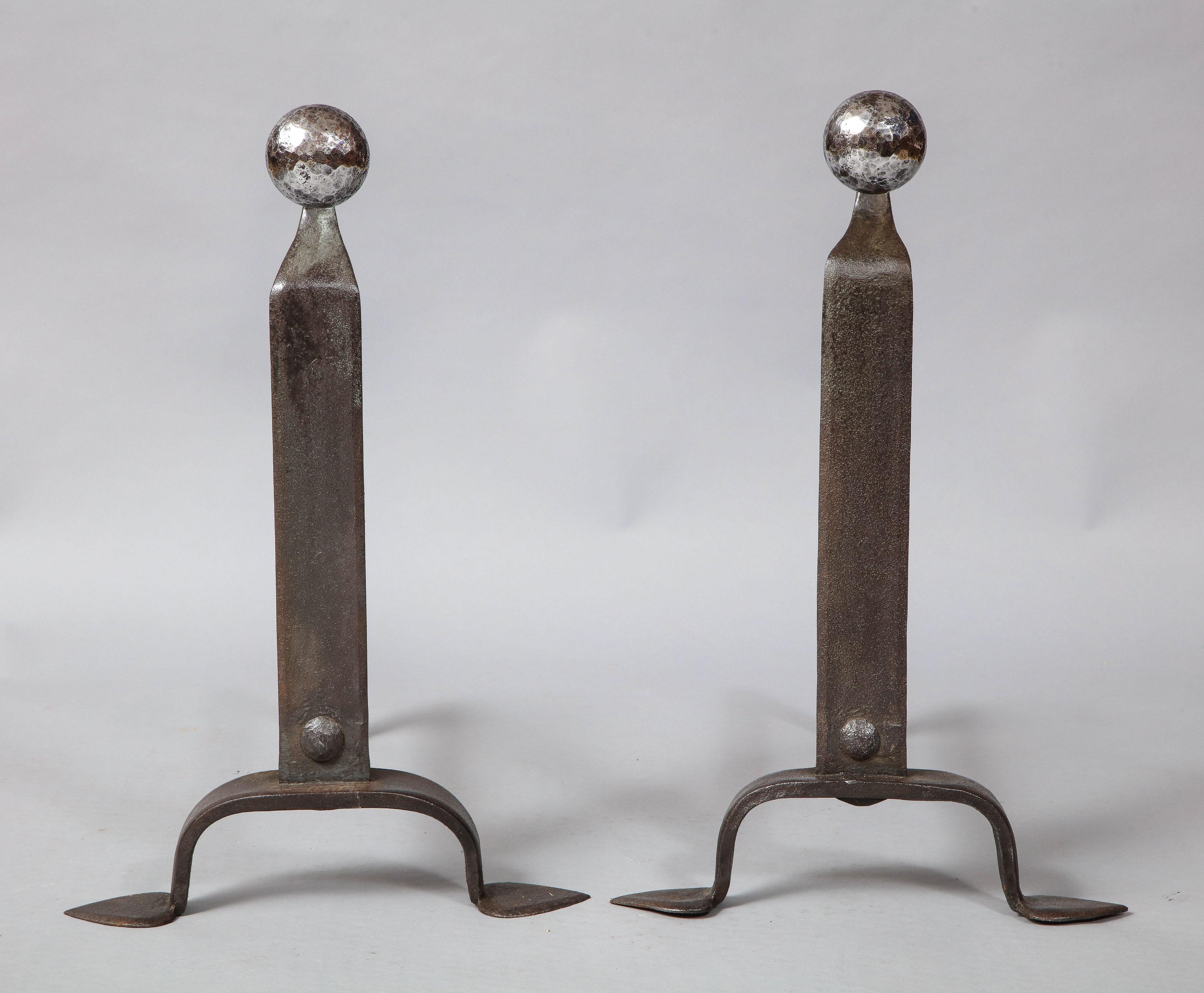 Very good pair of early 20th century blacksmith made andirons having bright polished steel hammered ball finials on goose neck shafts, the beaten iron body ending in shaped legs ending in spade feet, the reverse side with rows of spit support hooks.