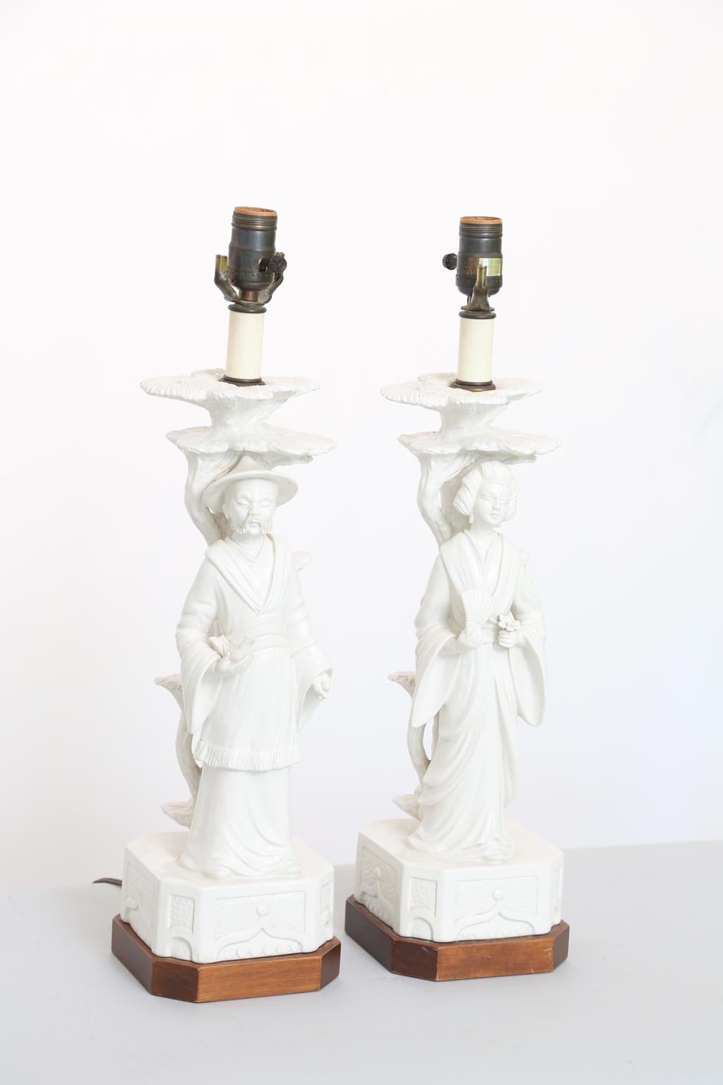 Pair of figural lamps, of Blanc de Chine style pottery, one a male in traditional dress holding a bird, the female holding a fan and lotus blossom, on square wooden base with canted corners. By Fredrick Cooper. 

Stock ID: D2675.