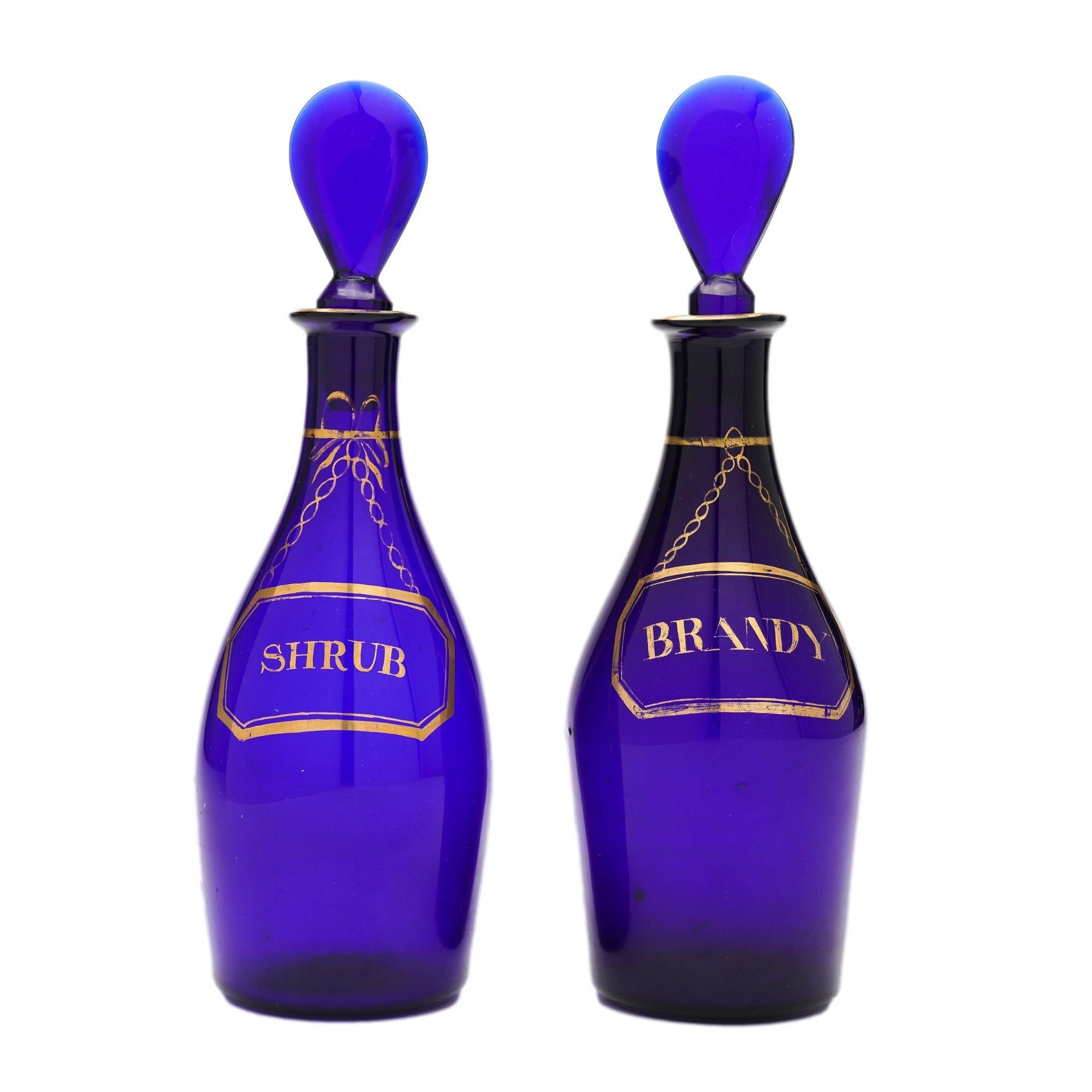 Pair of pyriform blown cobalt blue glass spirit bottles with mallet form stoppers and gilt decoration centering on identifying labels for Brandy and Shrub. Attributed to the studio of Isaac Jacobs.
Bristol, England, circa 1790-1810.