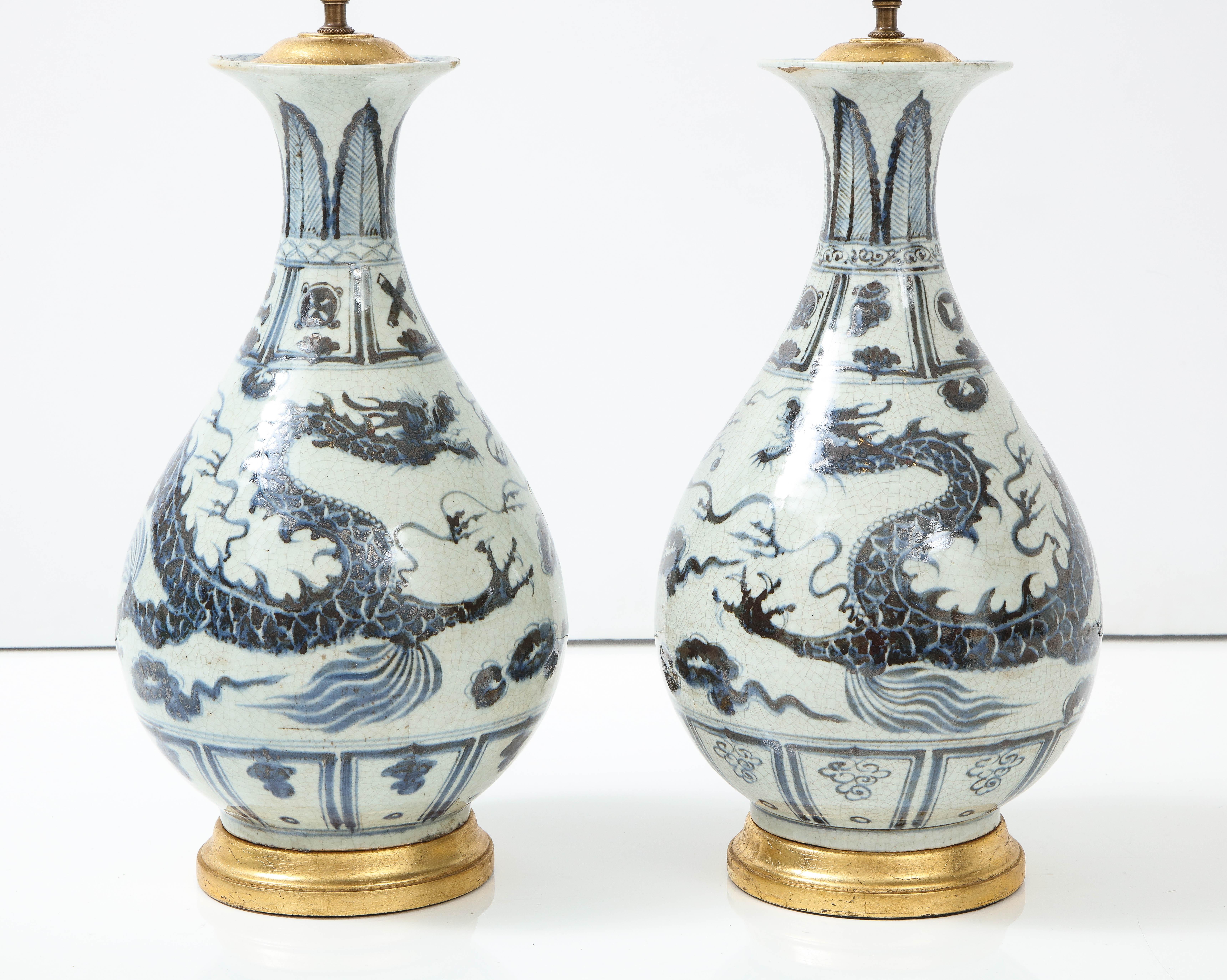 A pair of blue and white Chinese export porcelain lamps in a graceful urn shape mounted on a gilt base. Depicting a dragon motif design, these lamps almost read neutral and can been with any decor, modern or traditional.