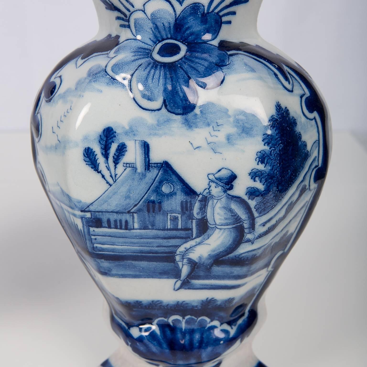 We are pleased to offer this pair of Dutch Delft blue and white mantel vases painted in shades of cobalt blue showing a well painted scene of a country gentleman seated on a bench near a cottage. The scene is bordered by a dark blue outline and