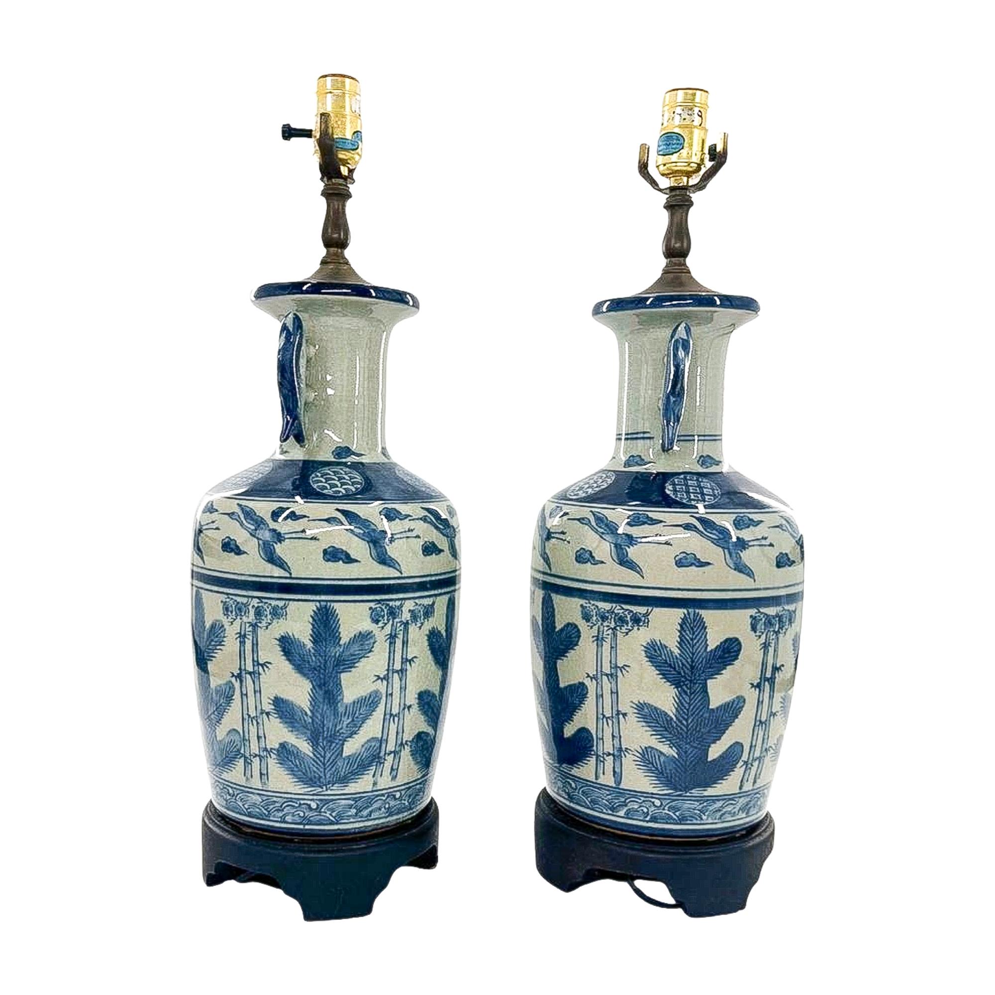 Une paire raffinée de lampes en porcelaine peinte à la main, chacune décorée de poignées sculpturales en forme de poisson et de panneaux représentant de gracieux hérons encadrés par des bordures géométriques nettes. La palette bleue et blanche est à