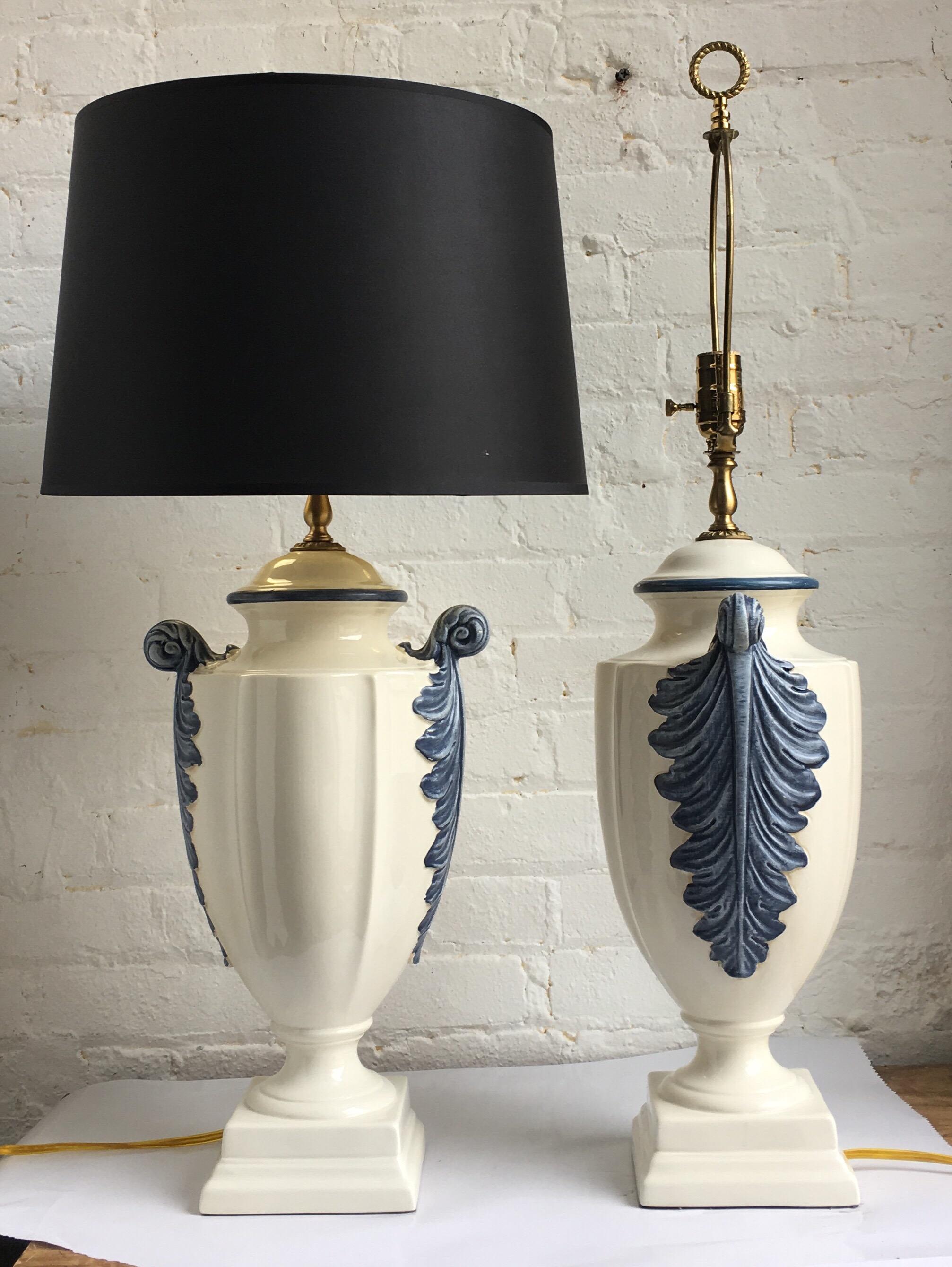 Pair of Hollywood Regency style blue and white porcelain glazed urn table lamps on plinth bases. Side handles feature dimensional hand painted plume or feather decorations. Lamp shades not included. 

Measures: 31.5 inches high to harp.
22.5