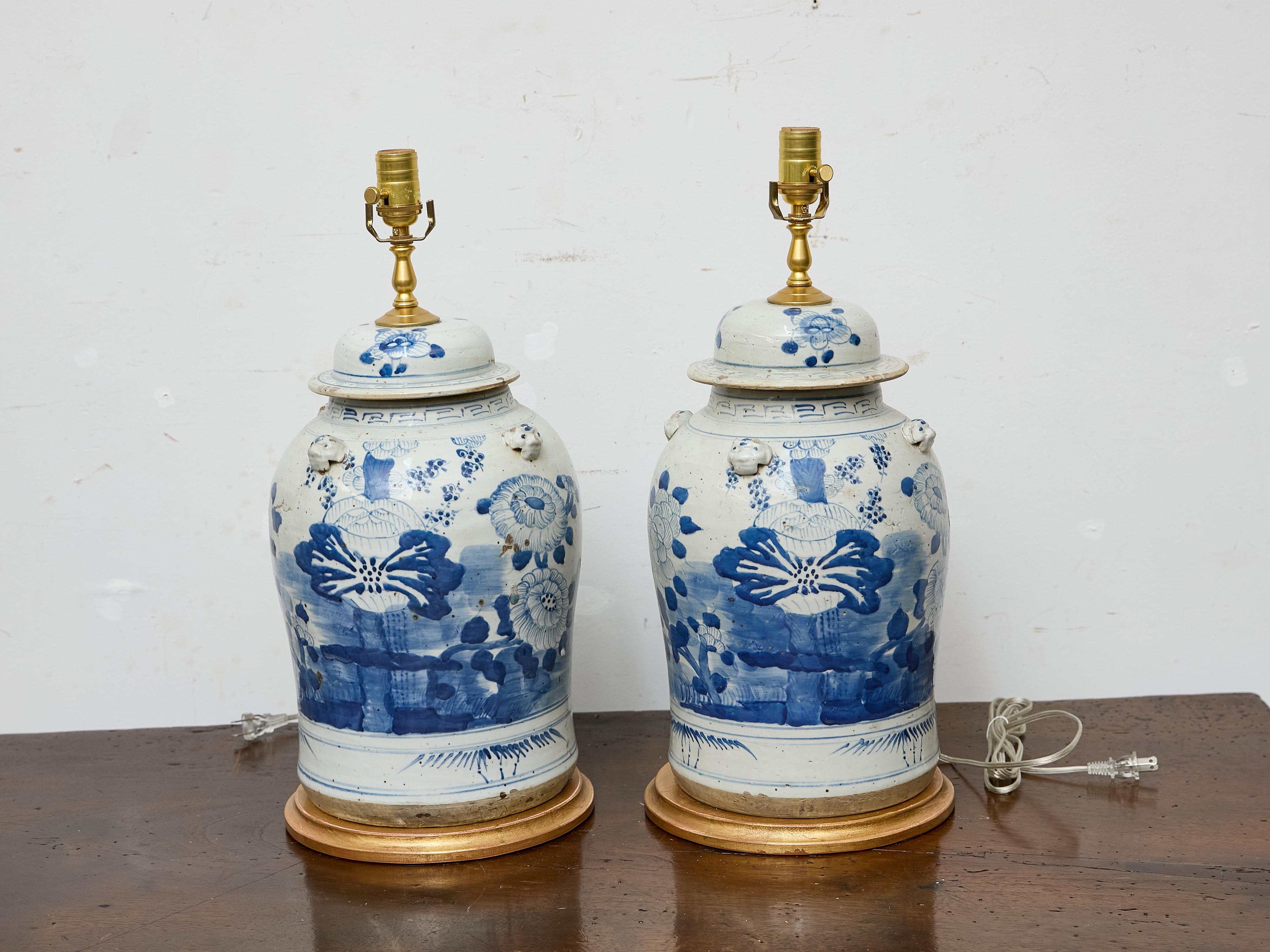 Ein Paar asiatische Porzellankrüge mit handgemaltem blau-weißem Blumendekor, neu montiert als Tischlampen auf runden vergoldeten Sockeln. Lassen Sie sich von der fesselnden Schönheit östlicher Kunstfertigkeit verzaubern mit diesem exquisiten Paar