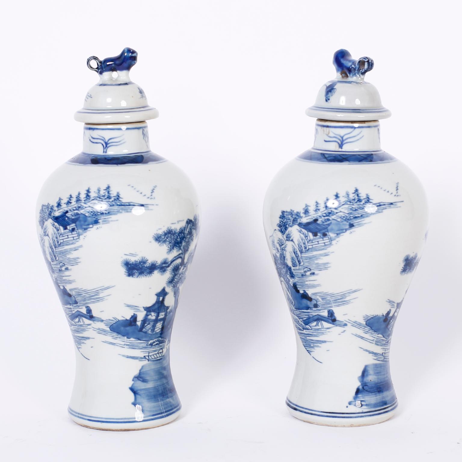 Pair of Chinese blue and white porcelain jars with foo dog handles and hand decorated with architectural landscapes all around.