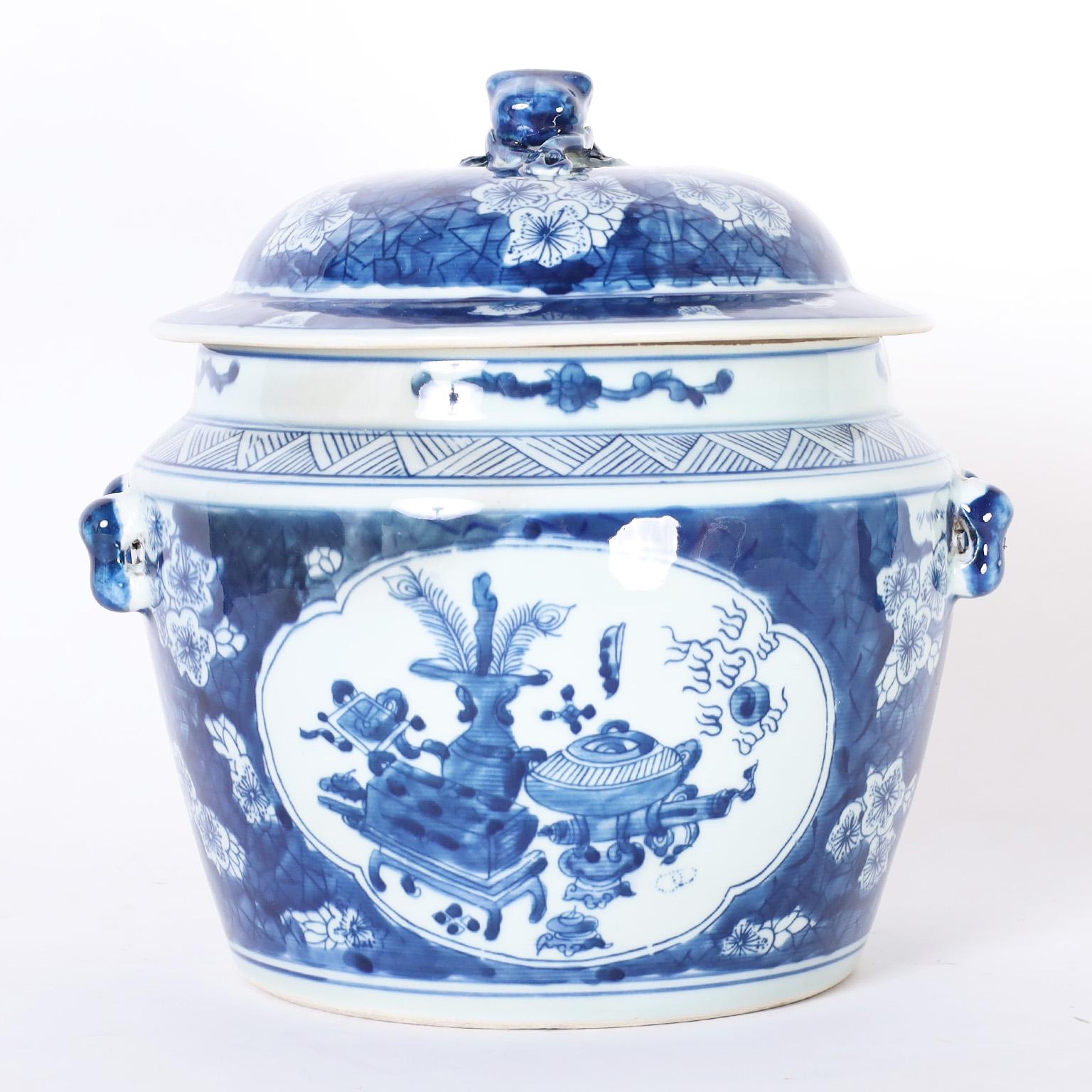Pair of Chinese blue and white porcelain lidded pots with figural handles and hand decorated with still life panels inside a blue background with flowers.