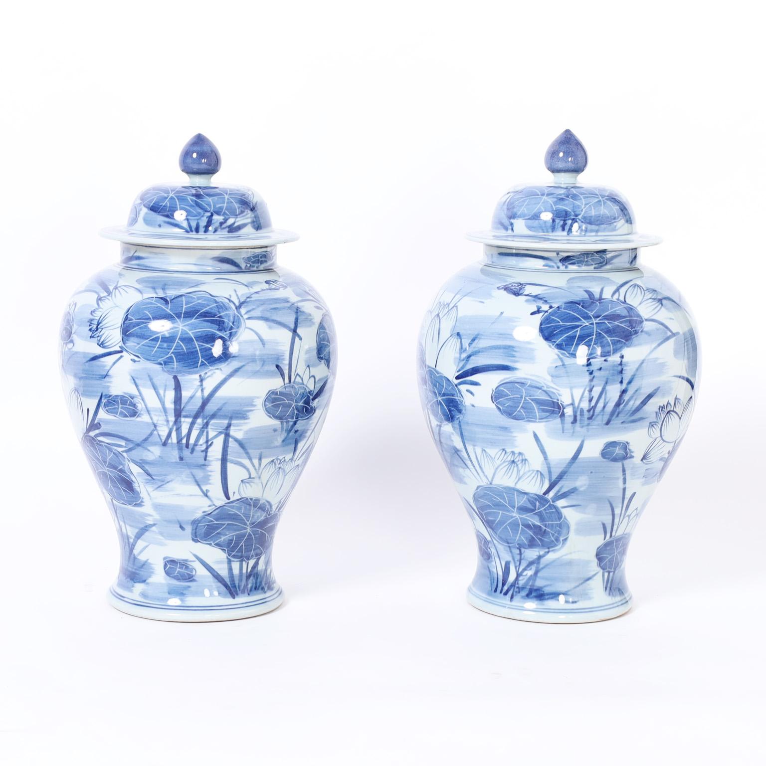 Charming pair of Chinese blue and white urns crafted in porcelain in a classic form with removable lids and hand decorated with lilies and flowers.