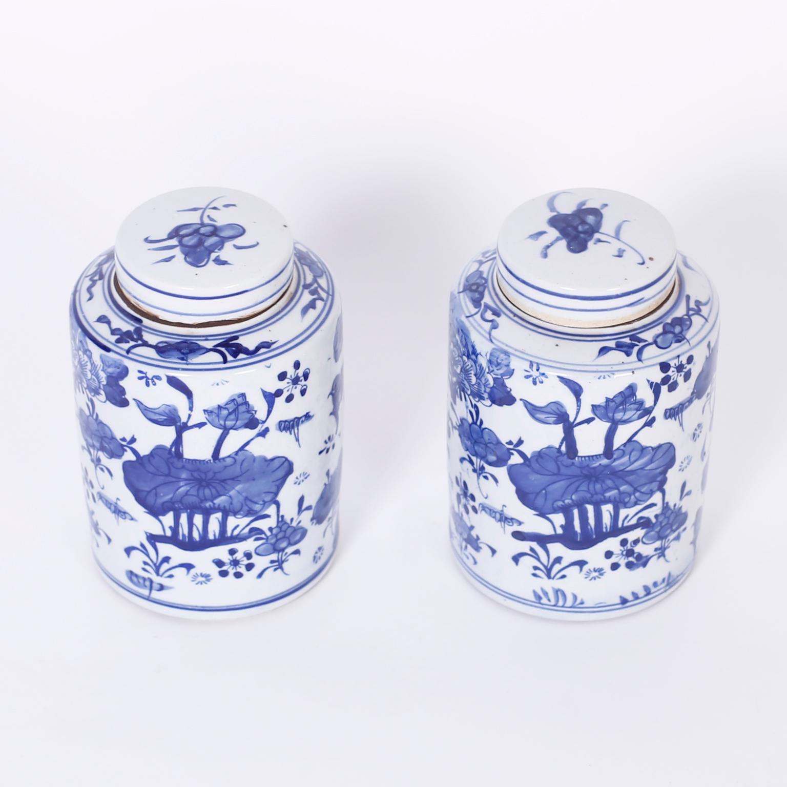 Pair of Chinese blue and white porcelain lidded tea jars with a cylindrical form and hand decorated with flowers and leaves.