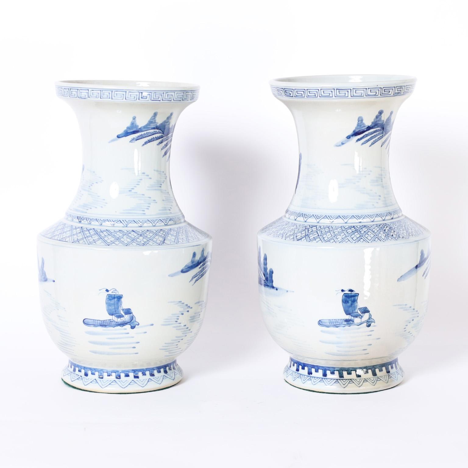 Pair of Chinese blue and white porcelain vases with classic form hand decorated with geometric borders and landscapes with trees and architecture.