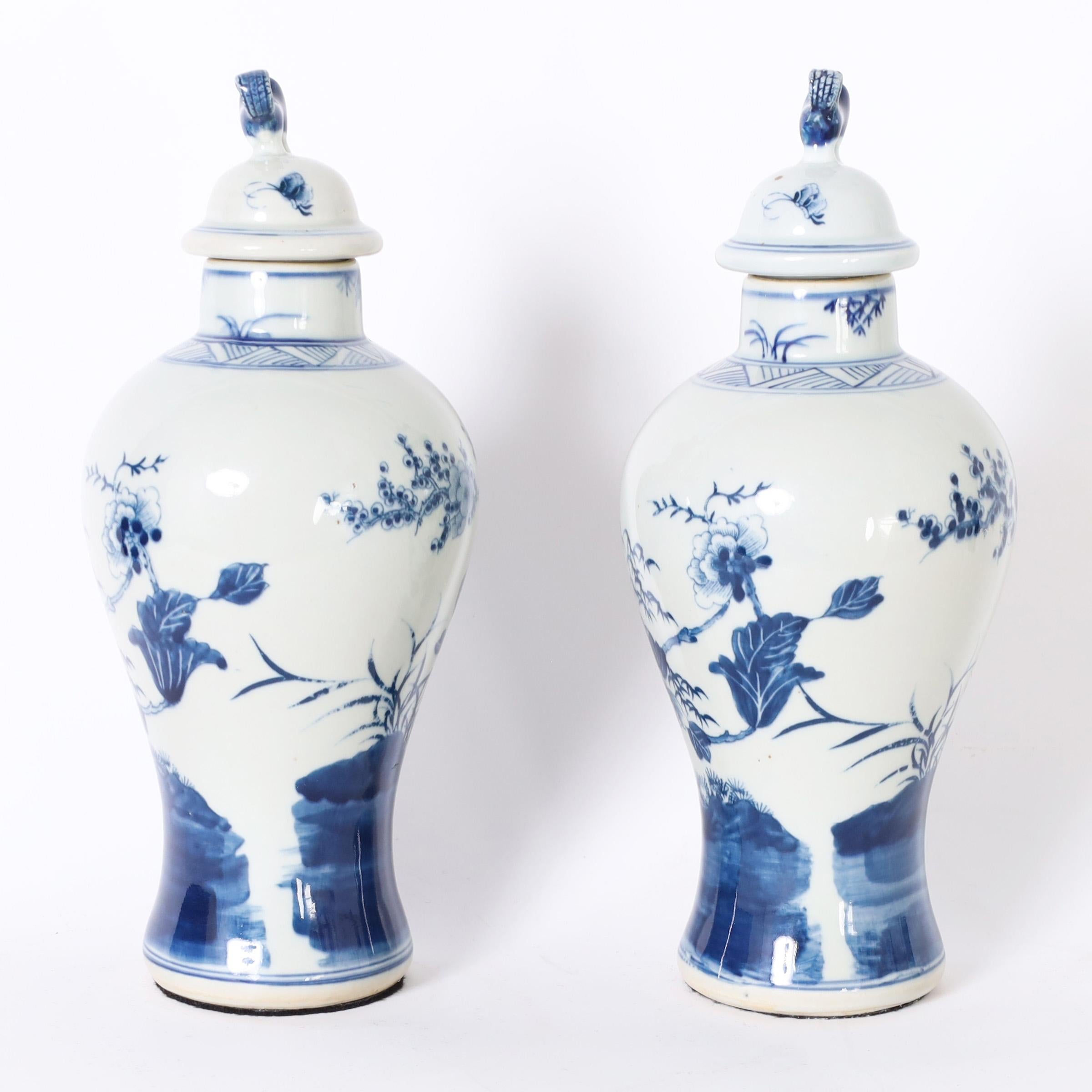 Lofty pair of Chinese blue and white lidded urns with classic form hand decorated with trees and flowers.
