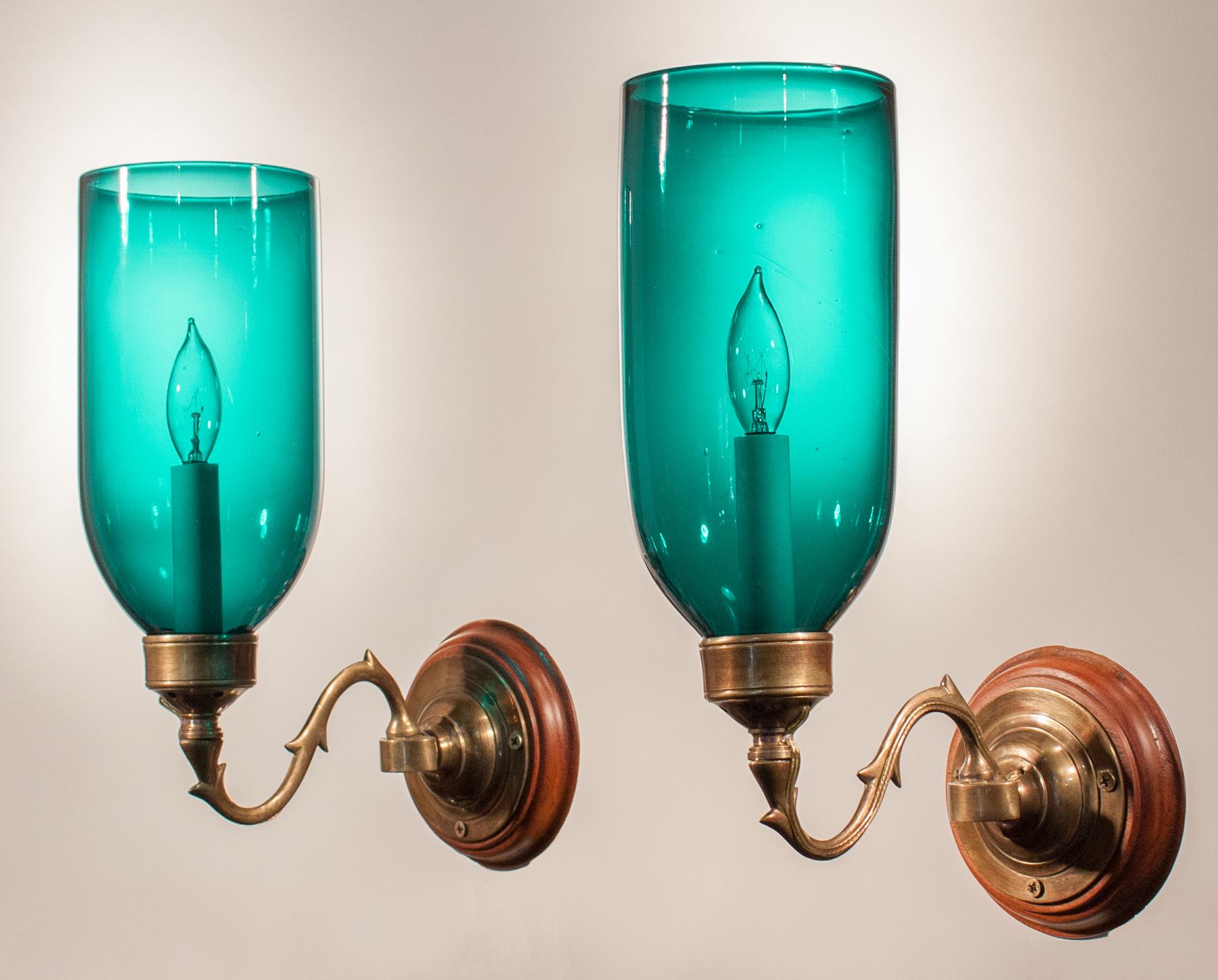 An exceptional pair of English hurricane shade sconces, circa 1860, with a teal green-blue hue. These authentic shades have desirable swirls in the handblown glass that speak to their quality and age. The wall sconces are newly electrified, each