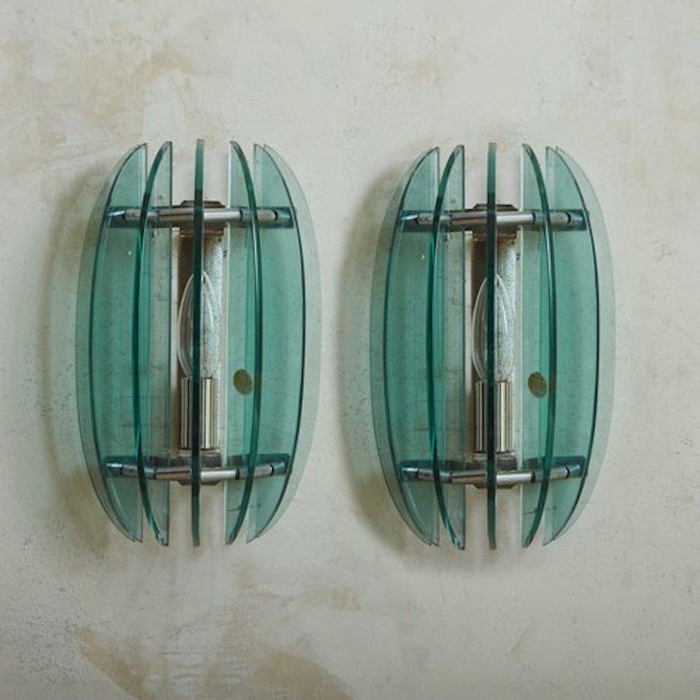 A pair of 1960s Italian sconces by Italian lighting company Veca. These sconces feature seven vertical demilune Murano glass panels in a beautiful blue hue. The panels are attached to a chrome frame and backplate. Retain ‘F.A.B.A. Pio Settembre’