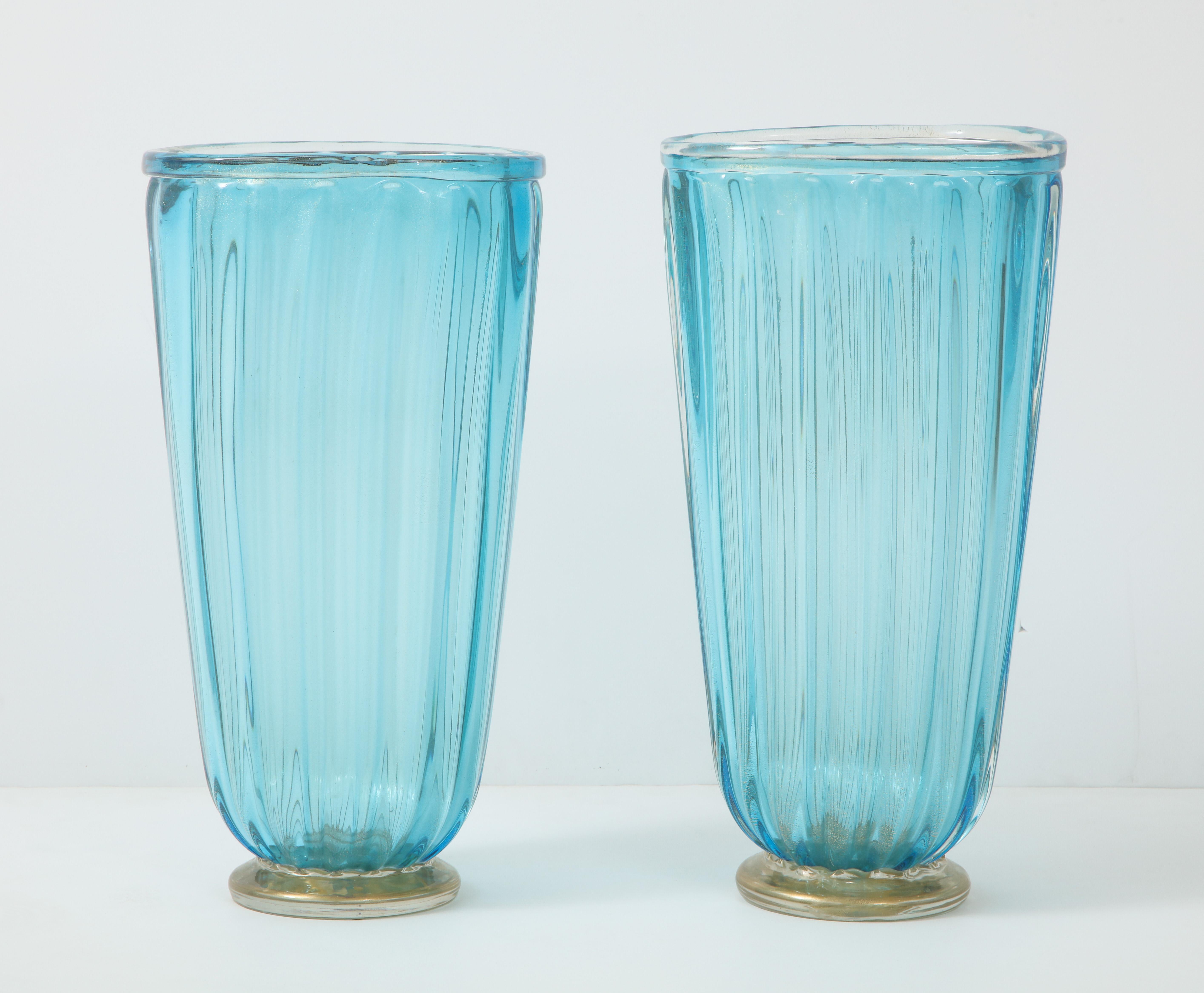 A pair of Murano glass vases in a stunning shade of blue. The round, fluted vases have a round base with gold leaf infusions. Perfect on their own or holding branches or flowers.