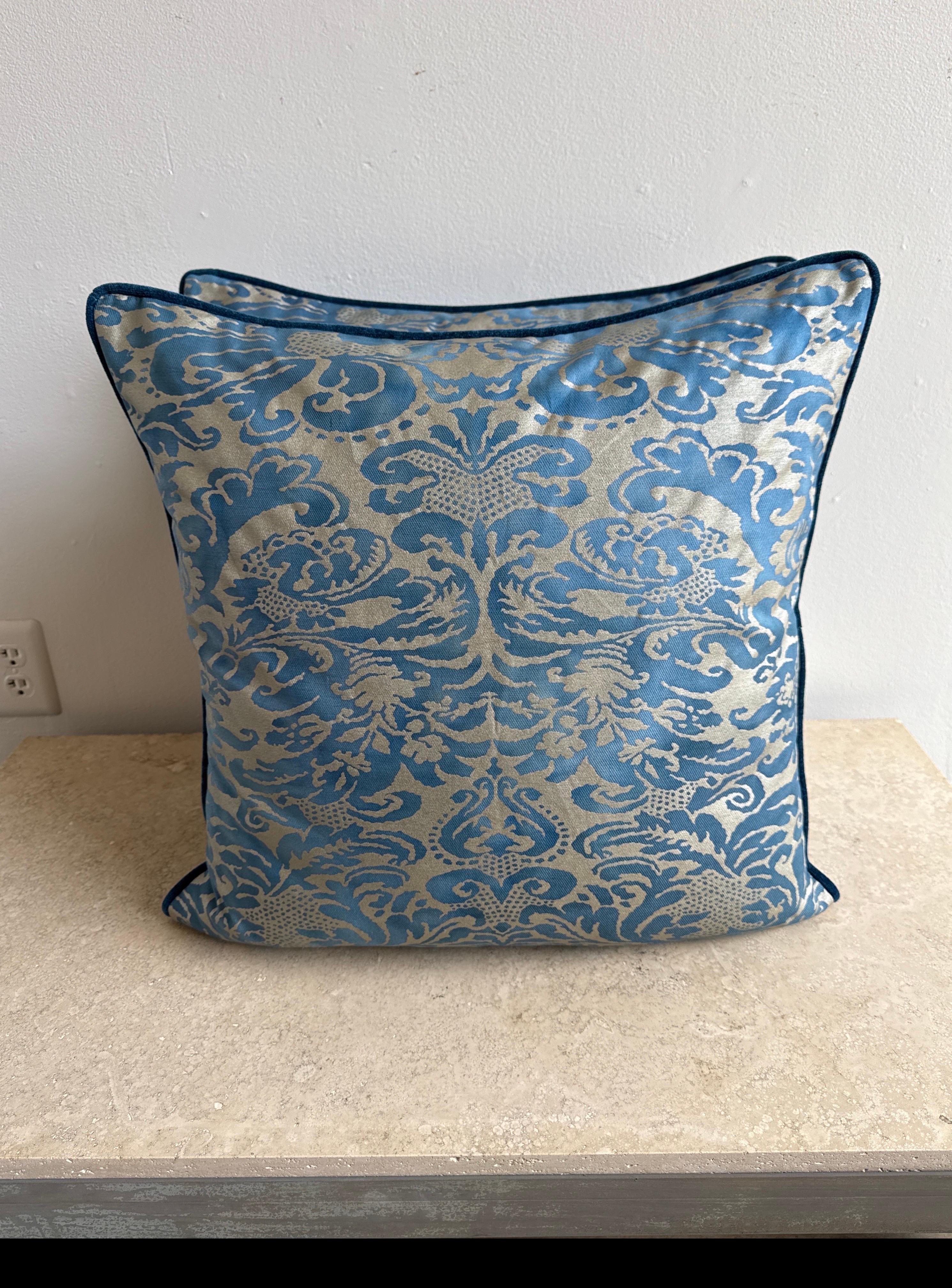 Estos elegantes cojines están confeccionados con el lujoso tejido italiano Fortuny, y muestran un rico motivo adamascado en tonos azules sobre un suave fondo beige plateado. El diseño atemporal es atrevido e intrincado, y ofrece una sofisticada