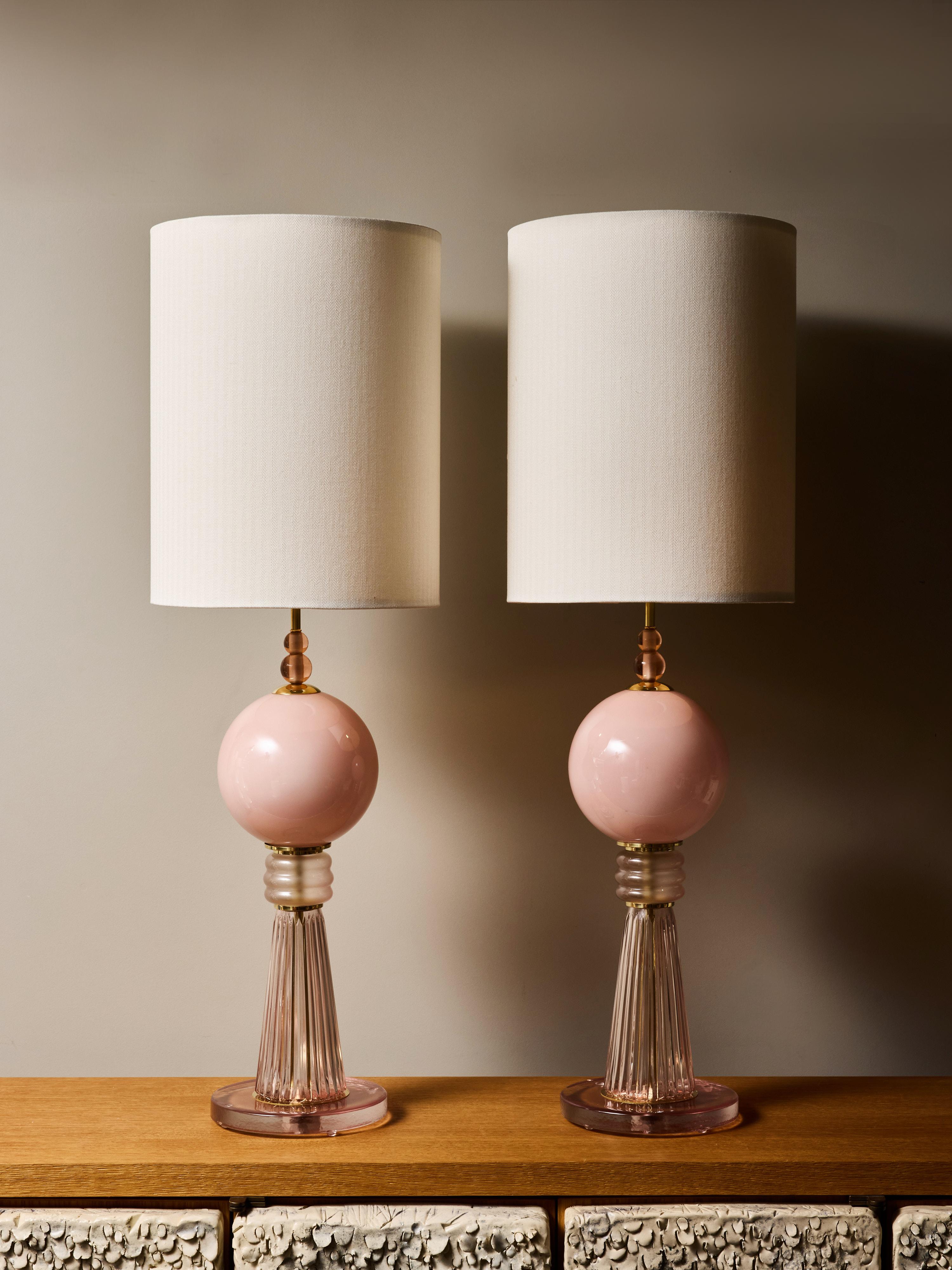 Una coppia splendidamente composta di lampade da tavolo contemporanee in vetro soffiato a mano, che sfoggiano un'elegante tavolozza di rosa arrossato e ottone caldo. Ogni lampada è caratterizzata da un sostanzioso globo di vetro rosa opaco che
