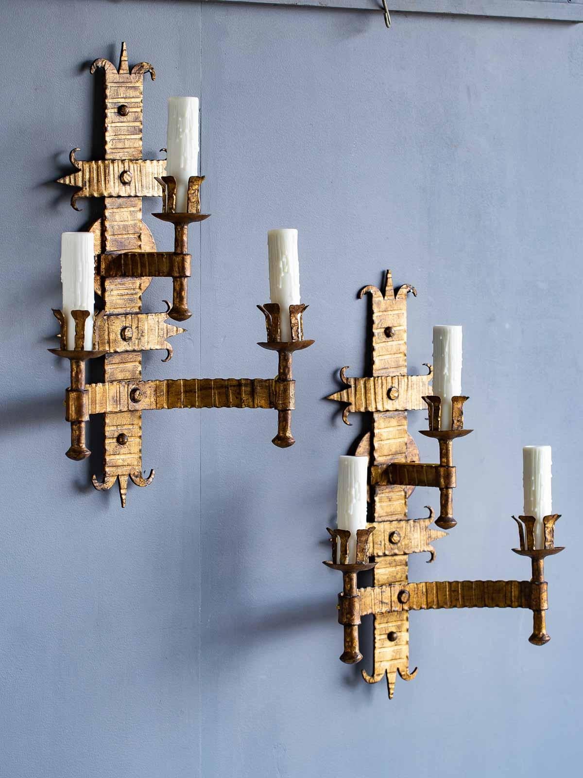 A pair of bold scale vintage French gilded iron two tier sconces, circa 1920 each having three arms and now electrified for in wall installation. Each strap of iron has a pattern forged into the material which was then welded into place before the