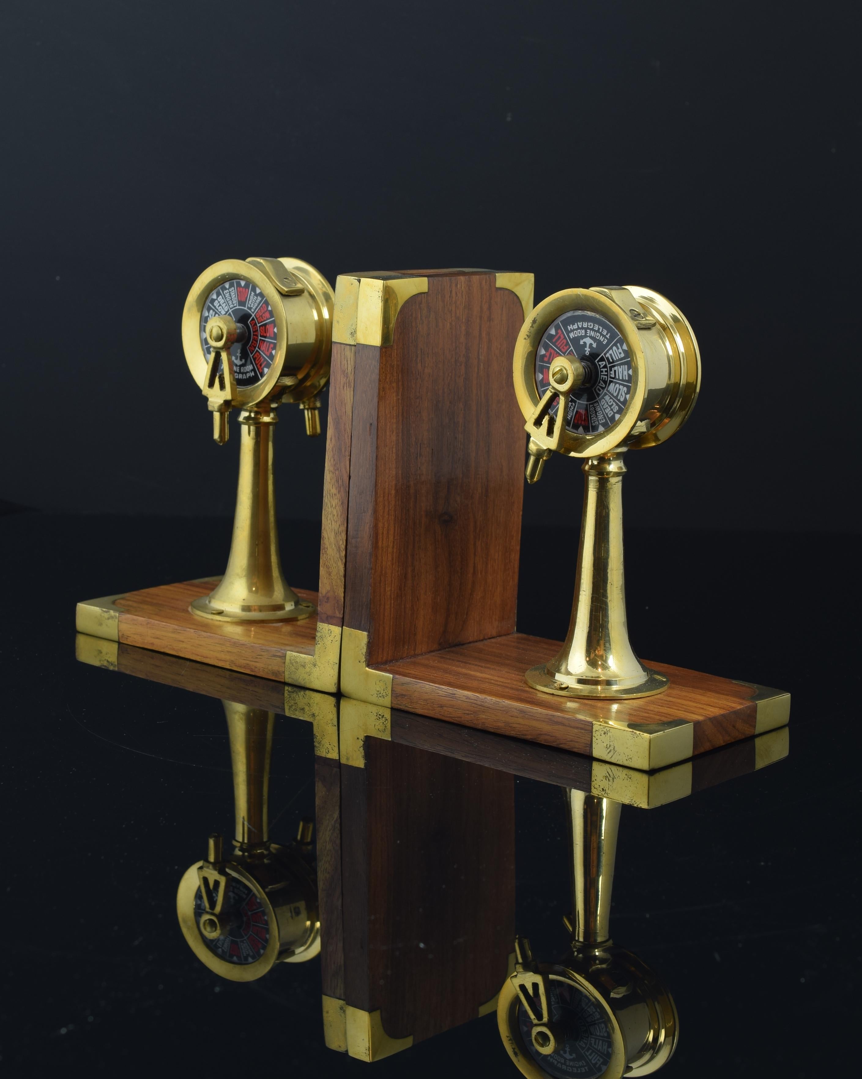 Pair of wooden and gold metal bookends.
 The decorative elements of these bookends have been placed on L-shaped wooden bases with the edges protected by metal plates. These elements reproduce on a smaller scale, in gold metal and the dial in black