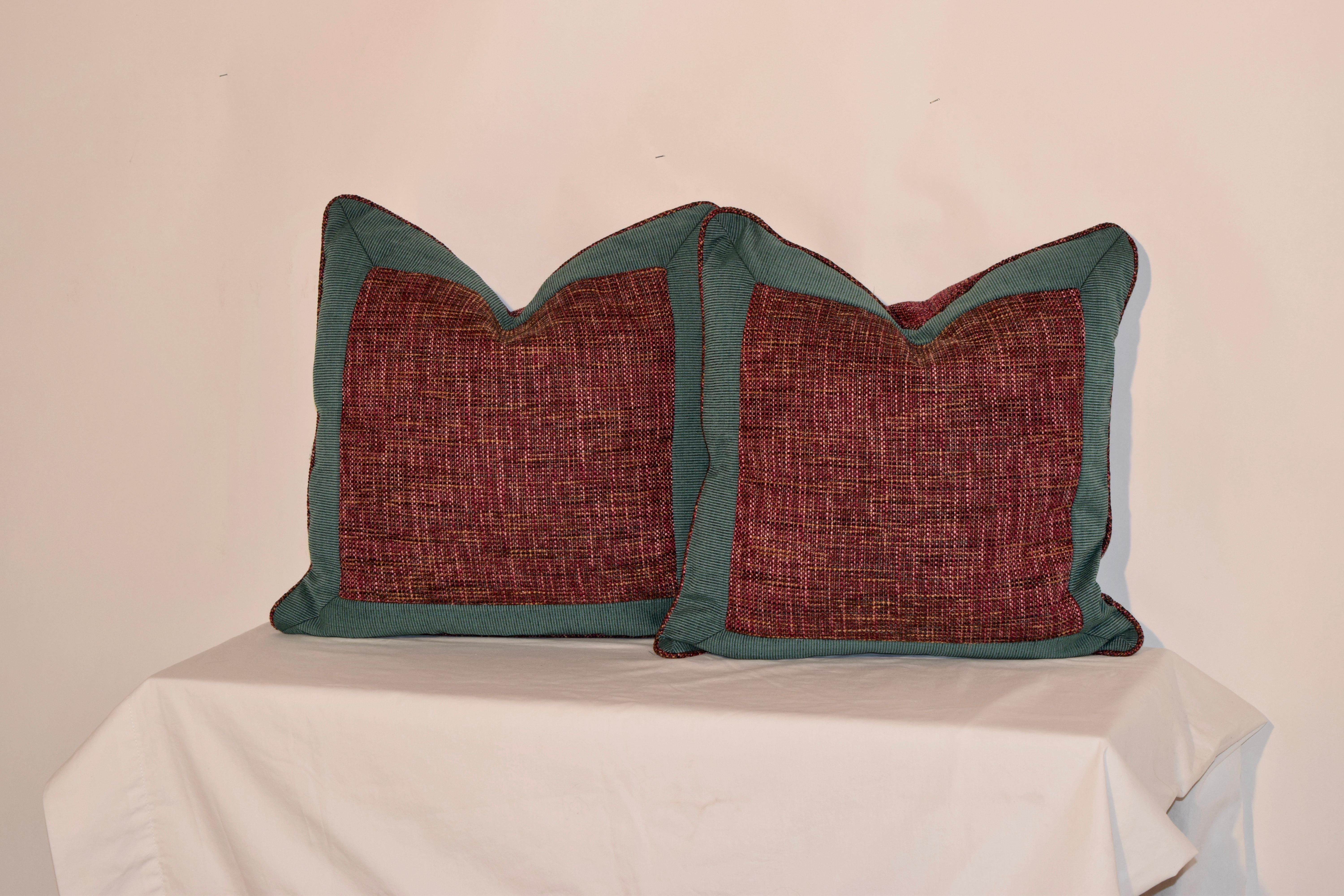 Handmade pillows with a teal faille border surrounding a central square of multicolored woven fabric. The back panels are made from the woven fabric, as well as the welt around the pillows. The pillow covers have hidden zippers and the feather