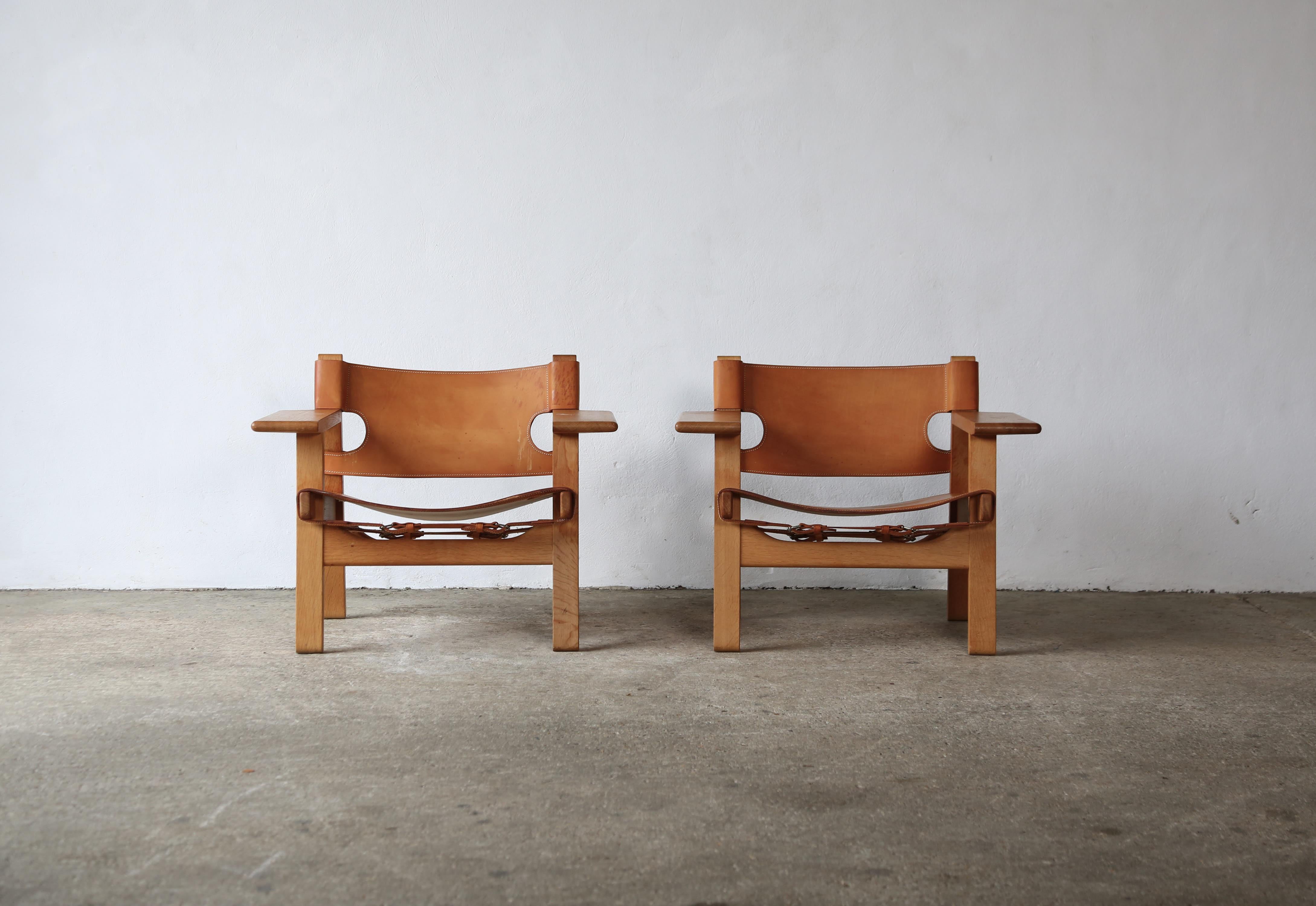 Pair of Spanish chairs by Børge Mogensen for Fredericia Stolefabrik, Denmark. Solid oak frame with natural saddle leather. The price is for the pair. Makers label to underside. Marks to the seat and some small marks to arms / frames as photographed