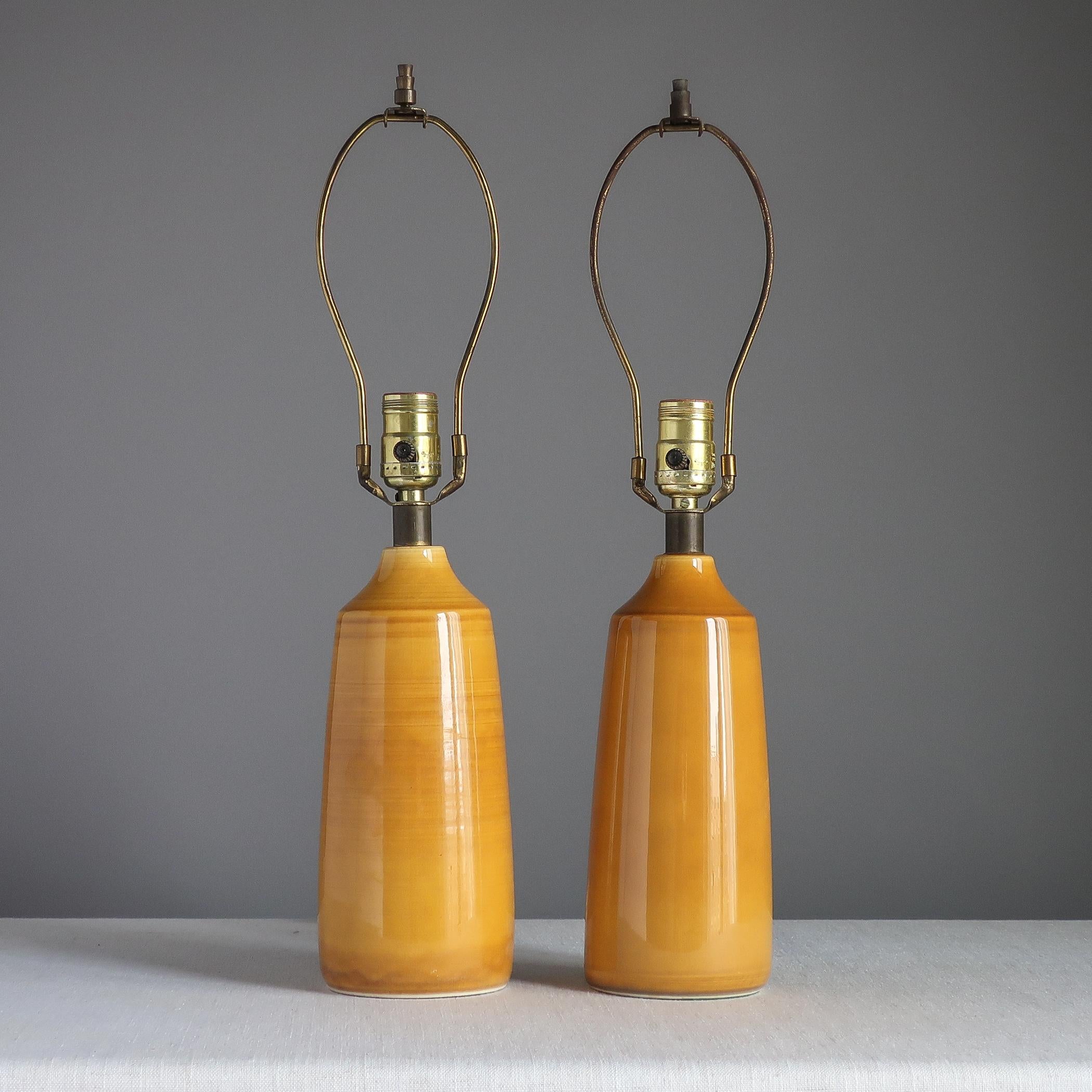 Pair of midcentury ceramic table lamps designed by Canadian/Danish couple Lotte and Gunnar Bostlund. Each simple stoneware body has a mustard-y yellow glaze. Bostlund label around cord hole at rear. 

Each ceramic base measures 10 inches high to top