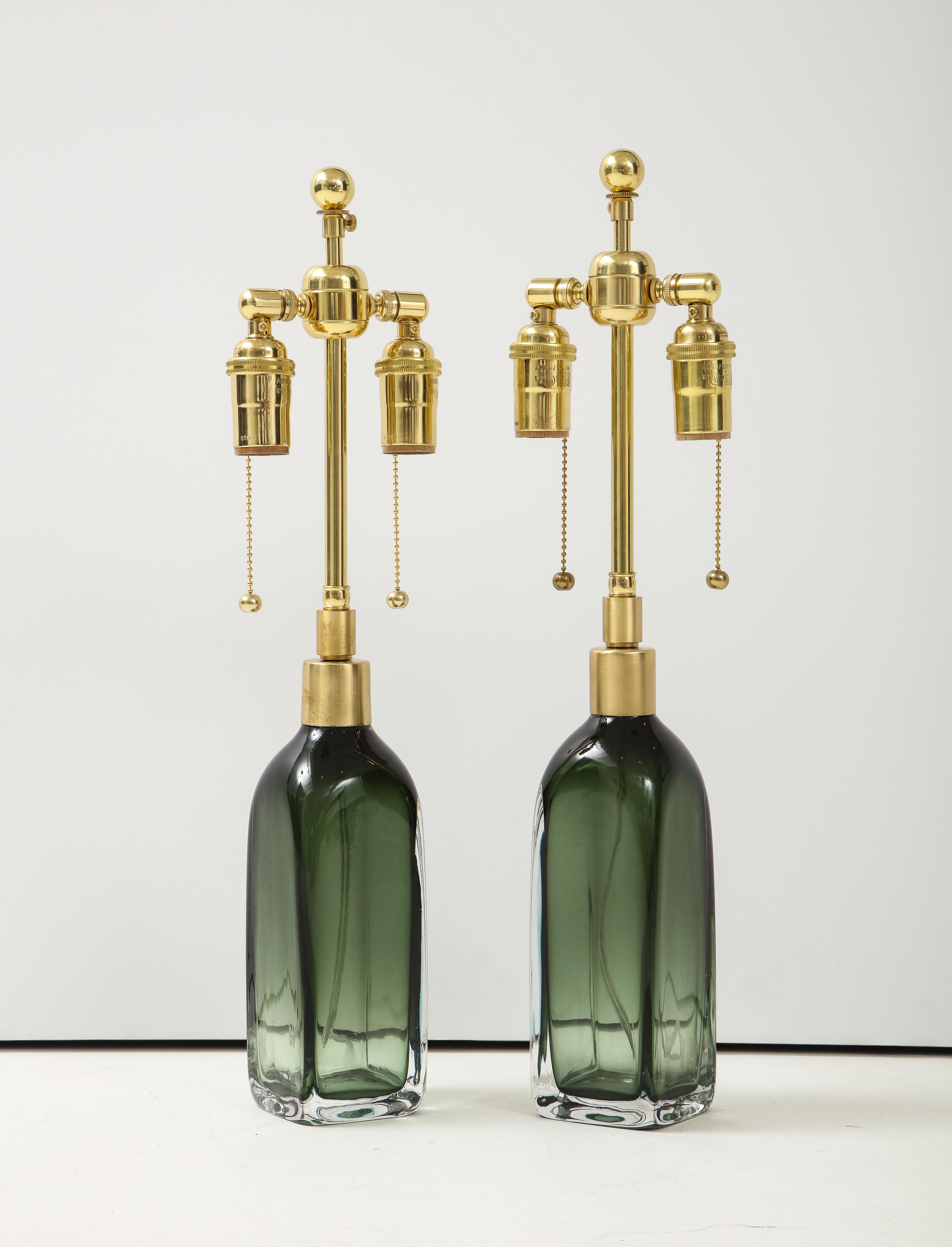 Pair of bottle green crystal glass lamps by Nils Landberg for Orrefors.
The lamps have been newly rewired with adjustable polished brass double 
clusters that take standard light bulbs.
One of the glass bodies is slight taller than the other but
