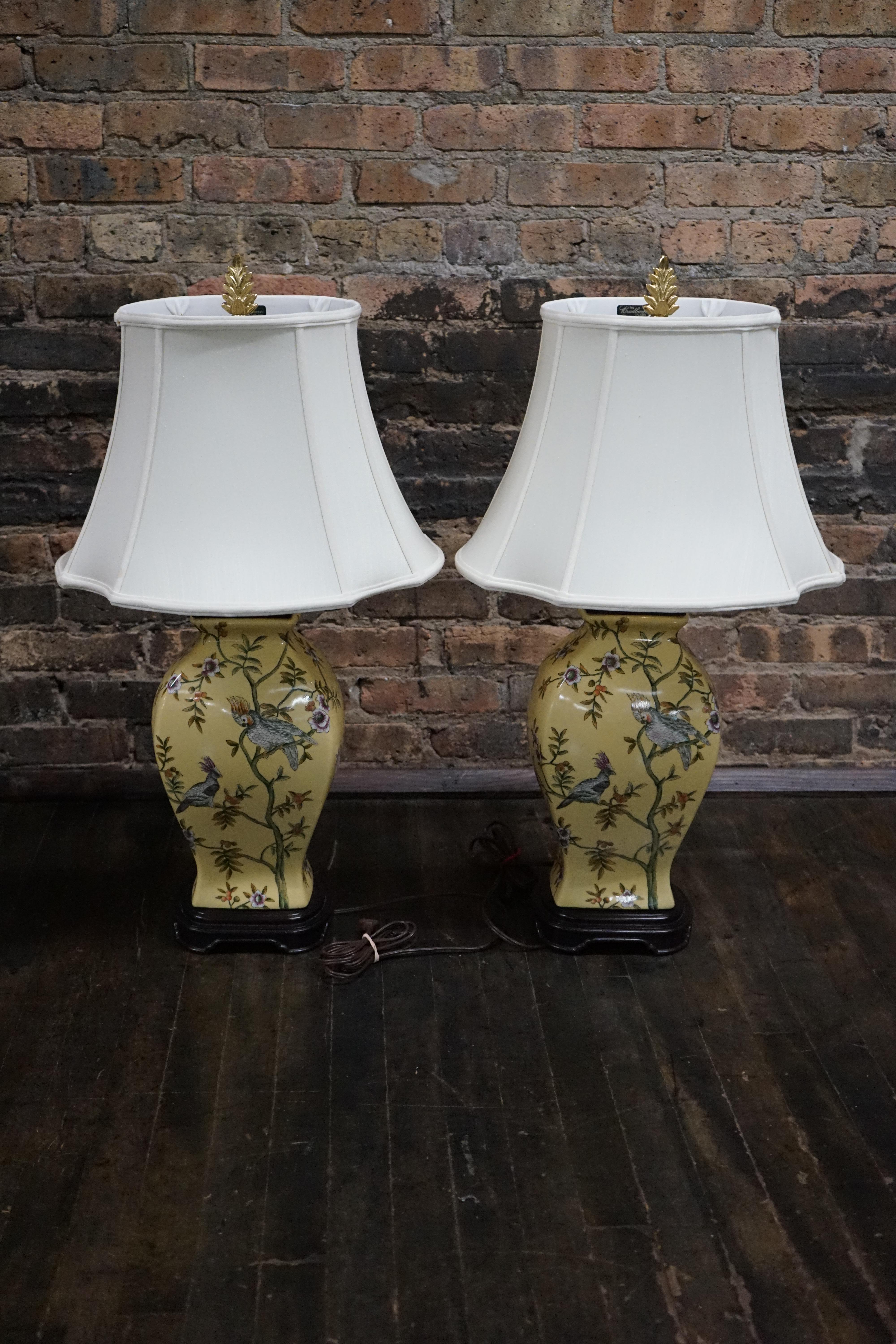 Lovely pair of matching hand painted ceramic lamps from Bradburn.  The urn shaped lamps sit on wooden pedestals.  The body of the lamp is a lovely shade of yellow and it is colorfully painted with flora and birds. Most of Bradburn's ceramic lamps