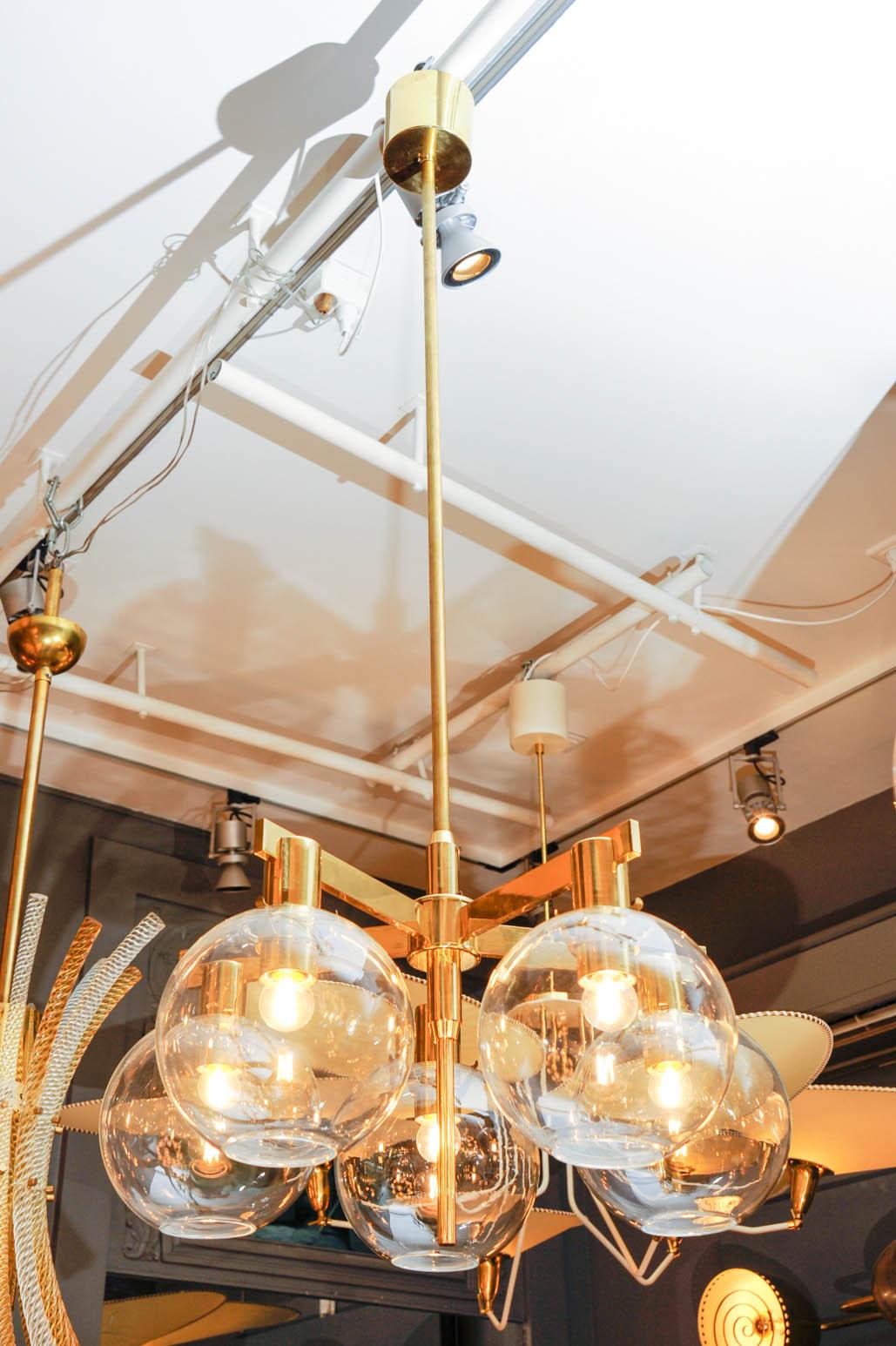 Pair of chandeliers by one of Scandinavian Modern most notorious designer, Hans Agne Jakobsson.

All in brass, long central stem with five arms each holding a clear glass globe.

Original sticker inside of each canopy.