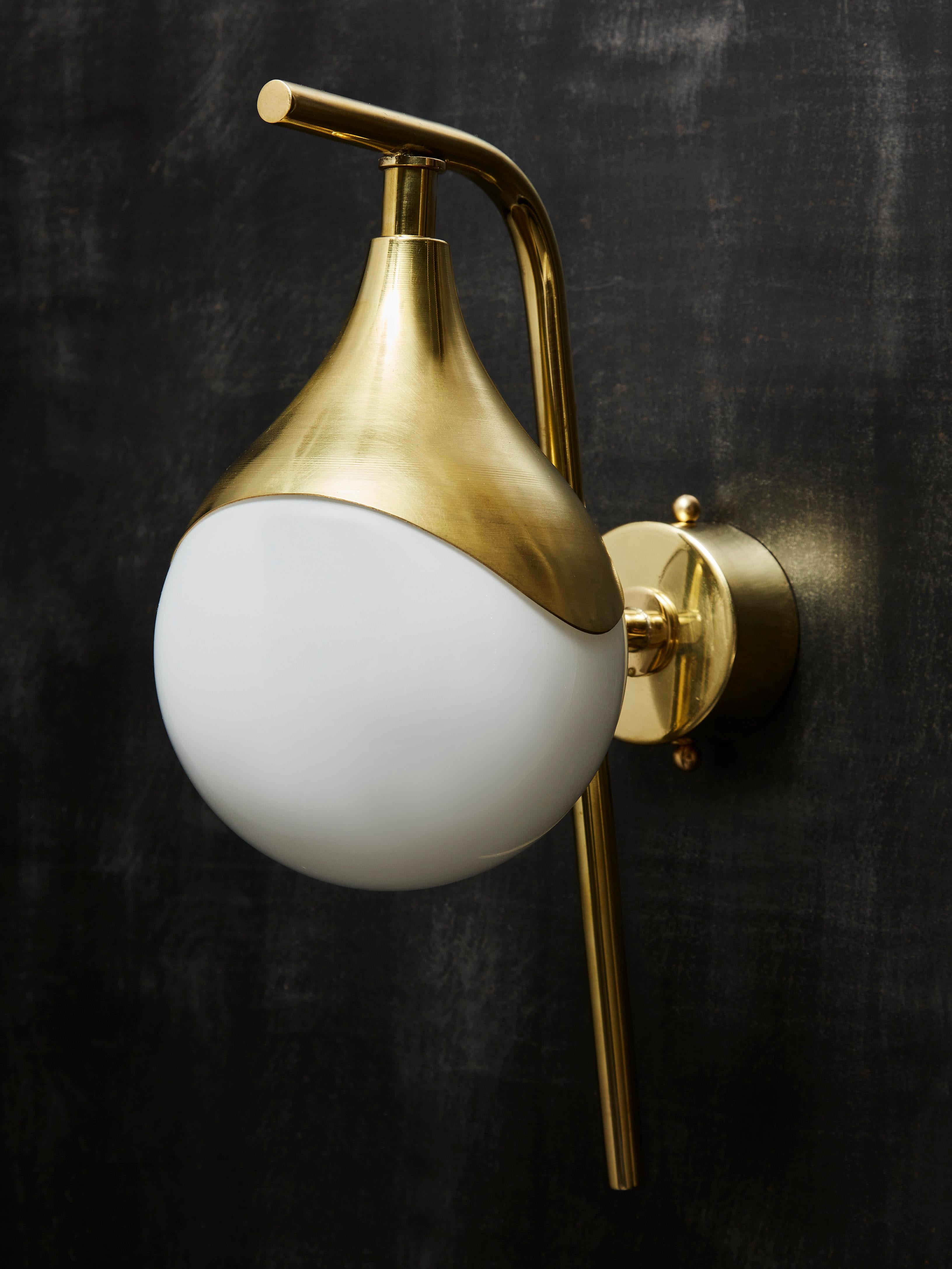 Pair of wall sconces each made of a brass L shaped arm from which hang an enlightened white glass globe.



Price displayed for a pair.