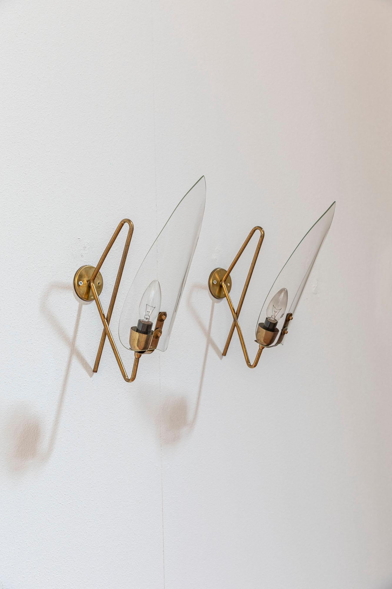 Geometrical brass structure and clear shade for an elegant and classy pair of wall lights.
