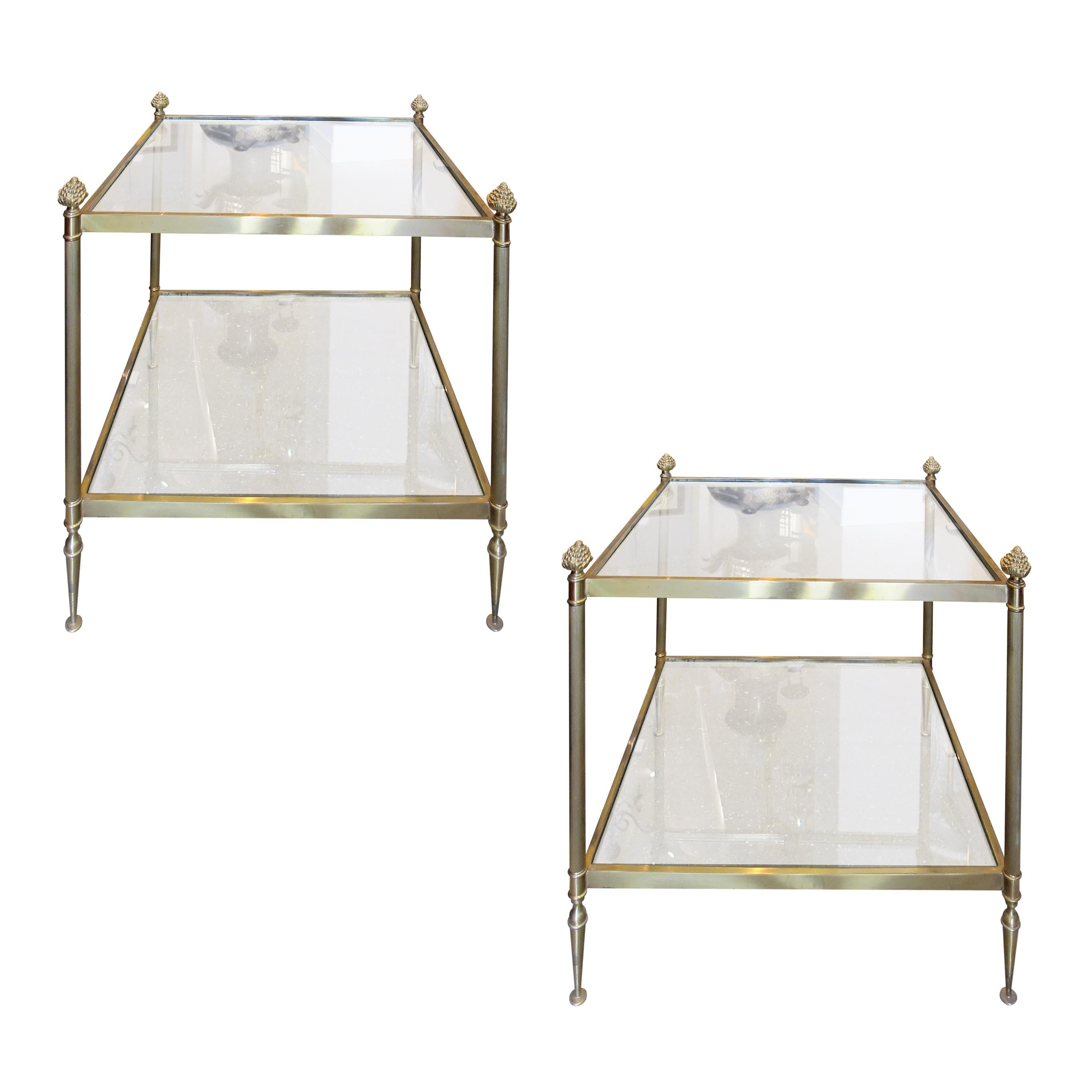 Elegant pair of mid-century French side tables in the style of Maison Bagues featuring brass frames with refined neoclassical details. Each table is designed with two tiers of glass shelving, supported by slender fluted legs capped with decorative