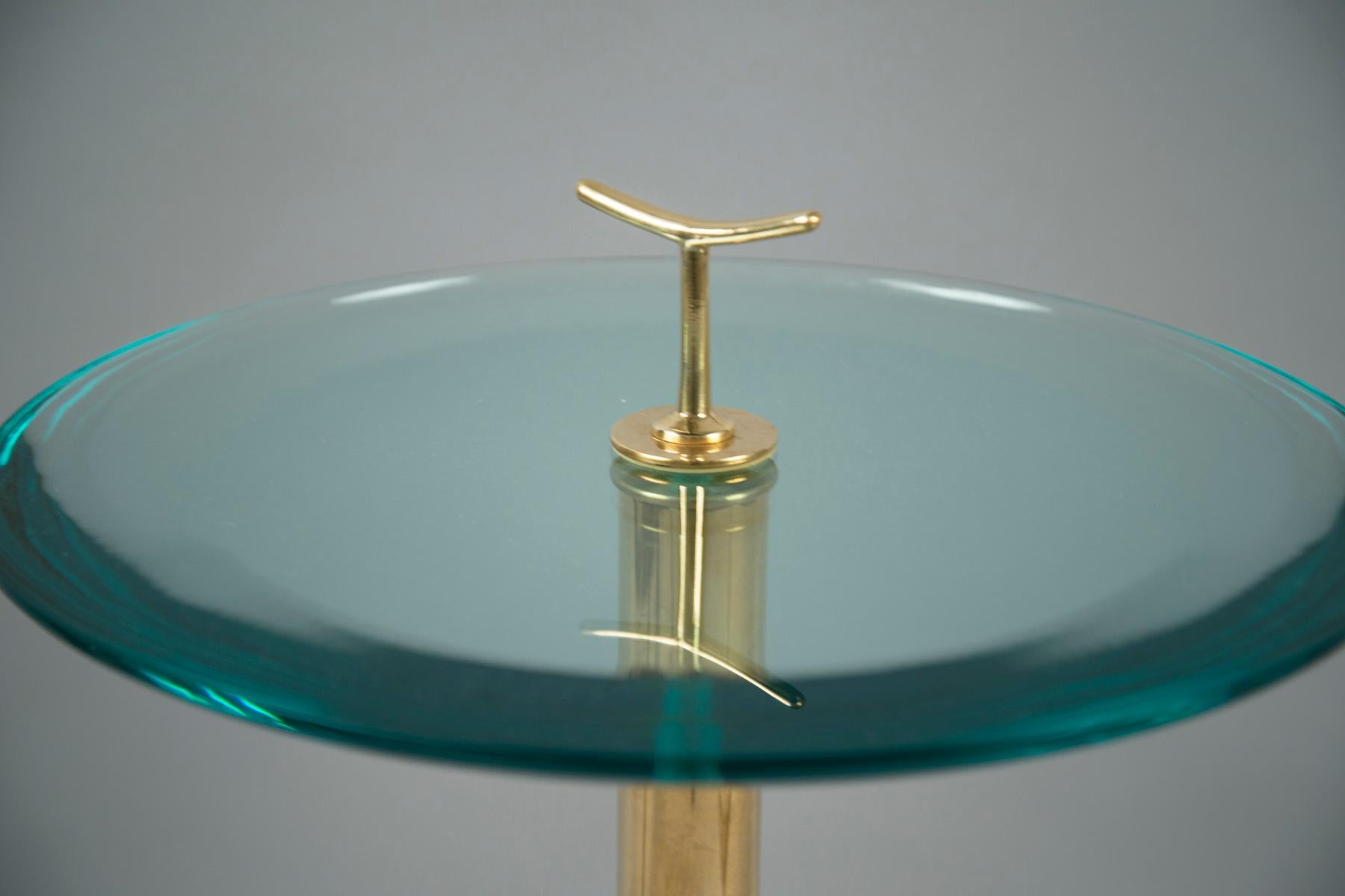 Brass stemmed side tables, each supporting a thick glass top with a green tint and a crescent shaped brass handle.

Overall height with handle: 26