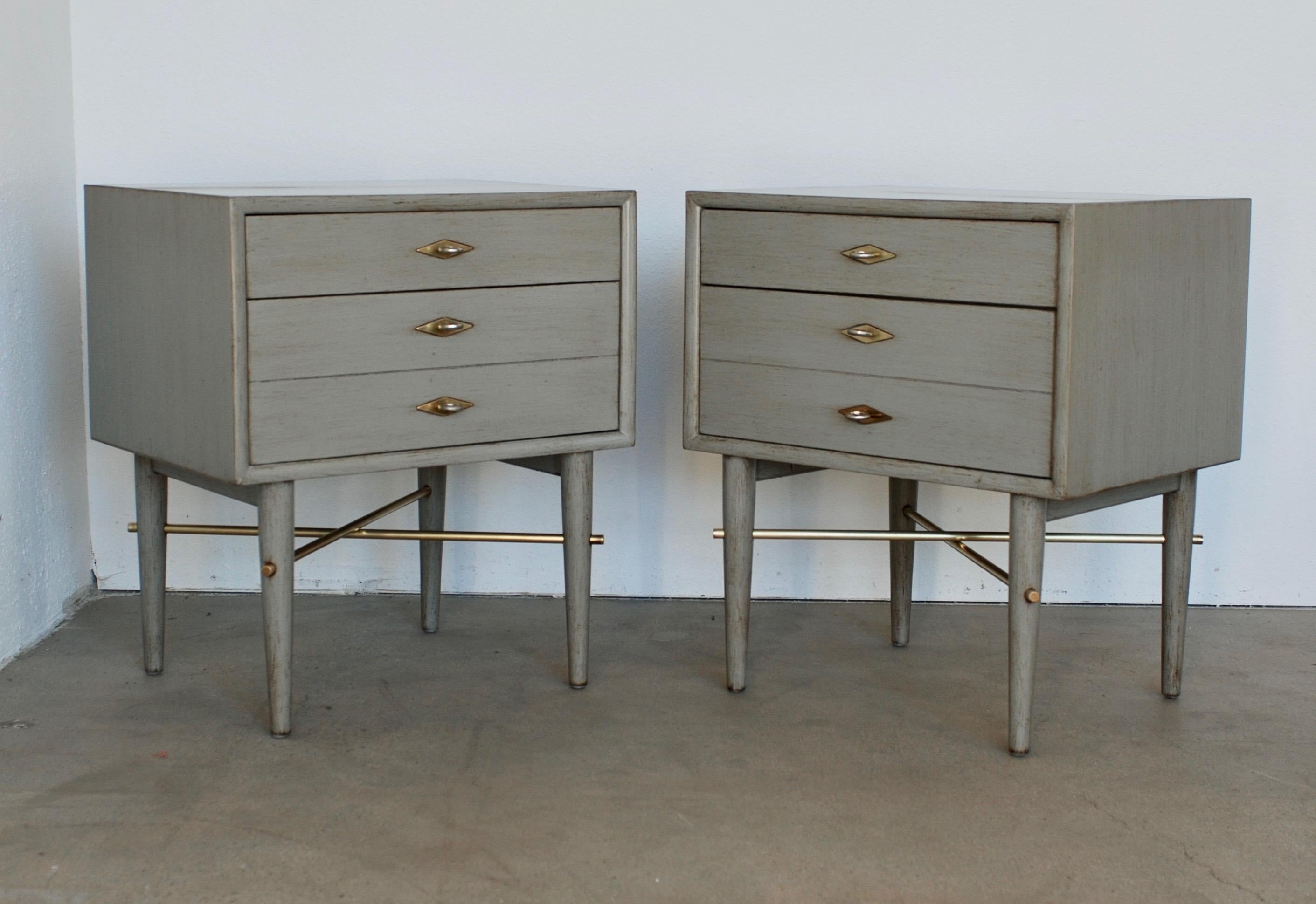 This pair of vintage American of Martinsville vintage nightstand have been refinished in a light grey with a dry brush finish to give the cabinets depth. There are brass cross bar fittings and brass backplates for the nickel colored hardware for a
